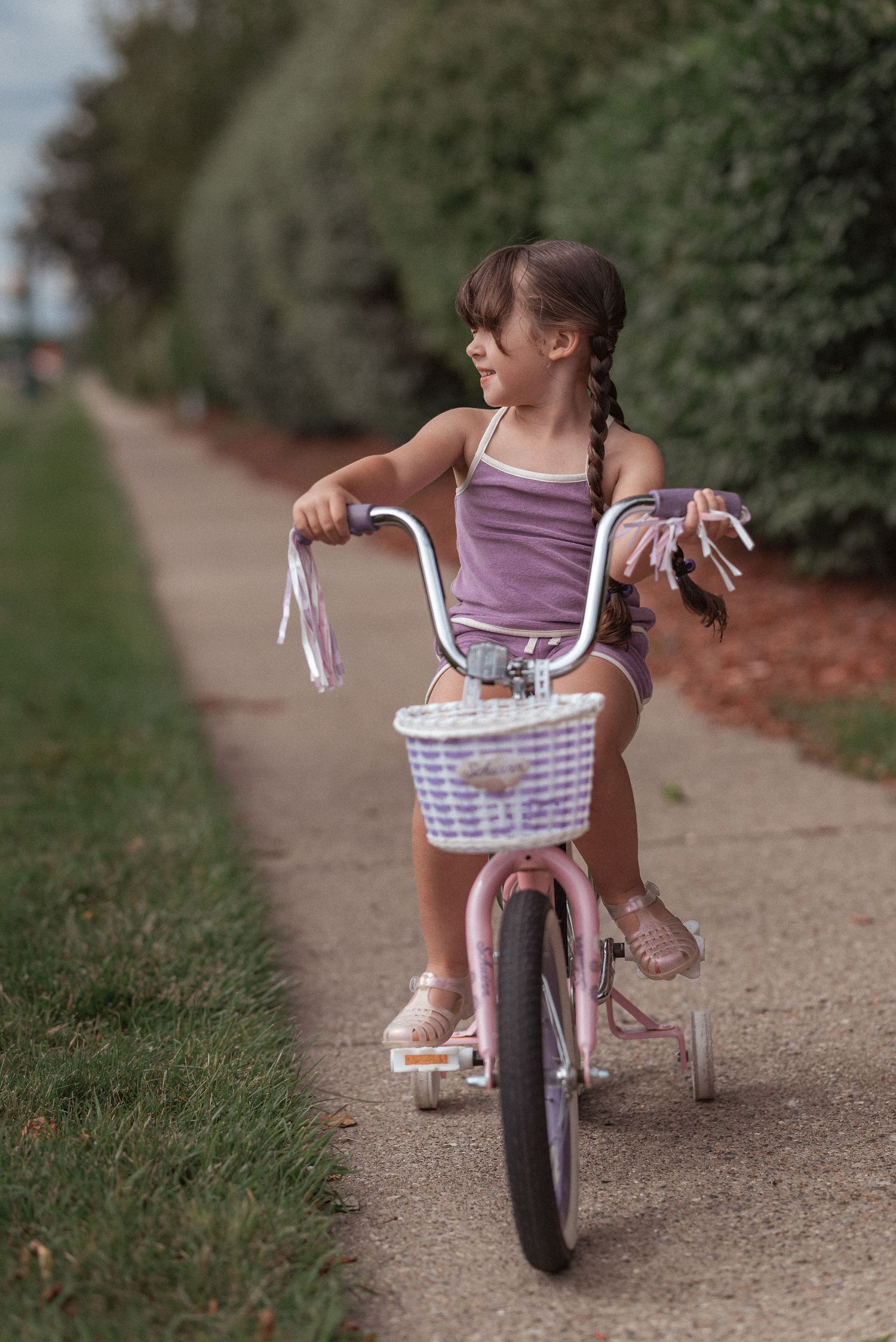 A child in pink rides a small bicycle with a white basket along a peaceful dirt path on a summer day.