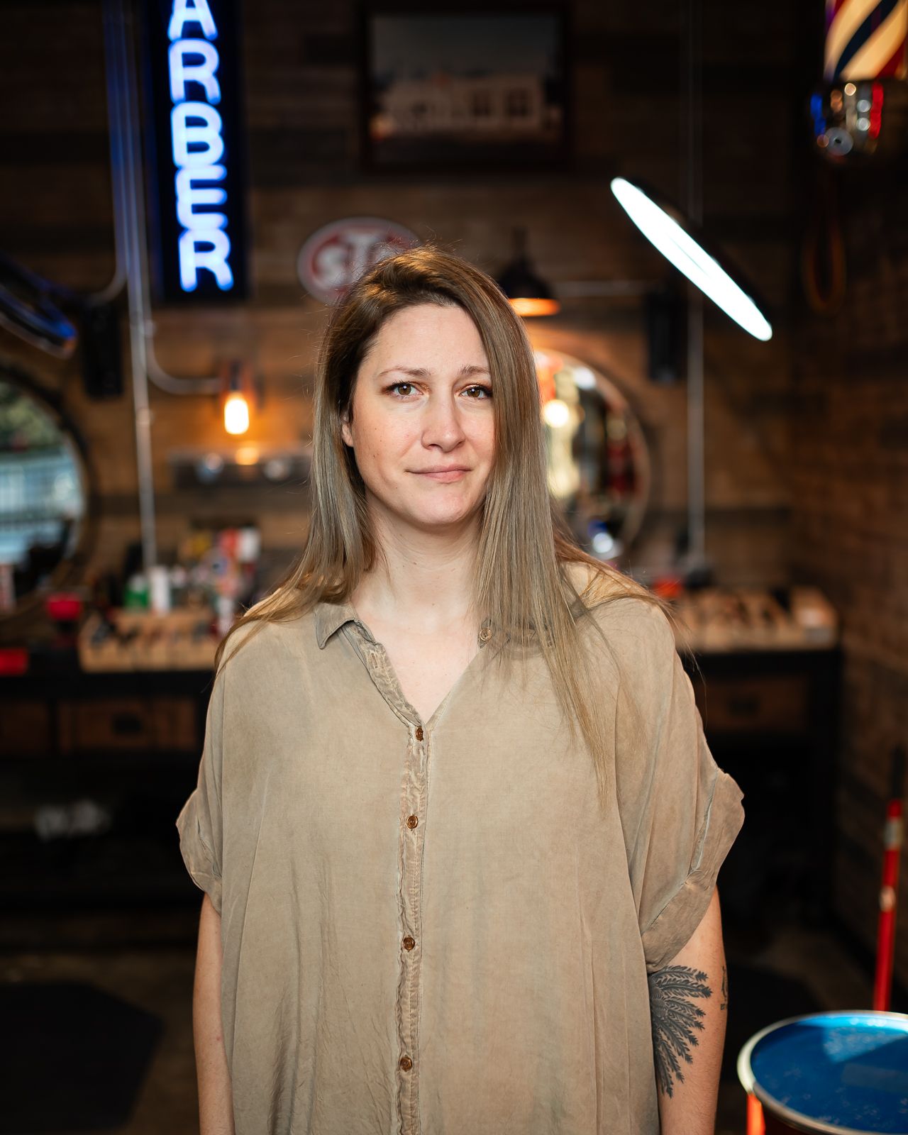 A person in a beige button-up blouse poses in a dimly lit restaurant setting.