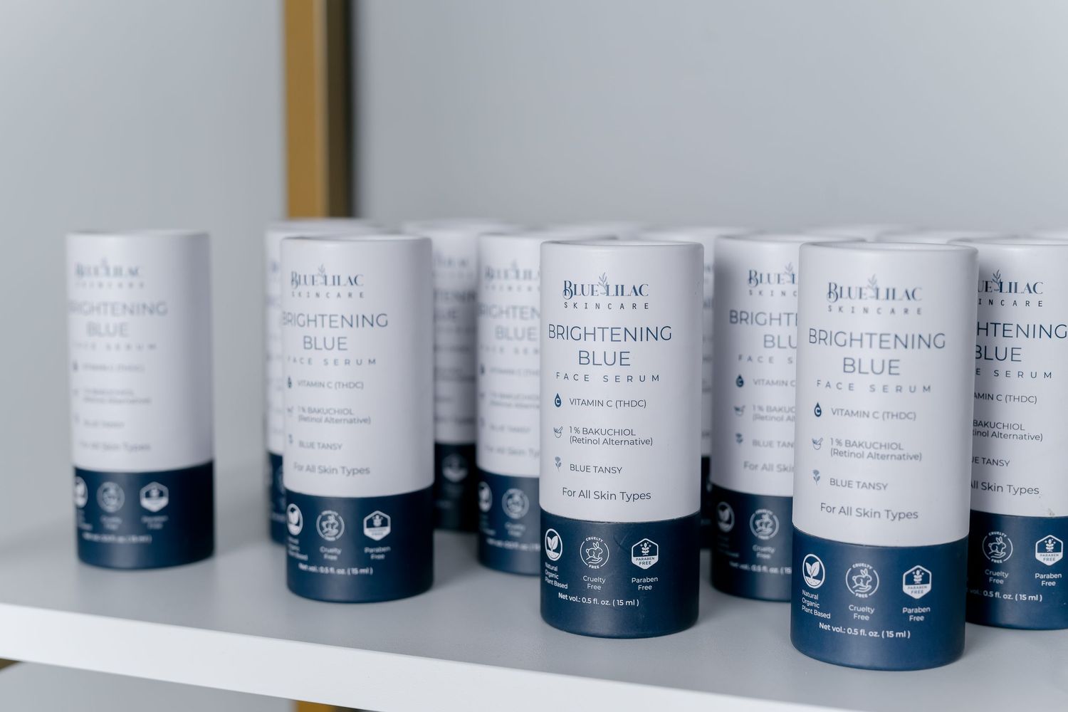 Multiple Divinity Skincare Brightening Blue Face Serum cylinders displayed on a white shelf.