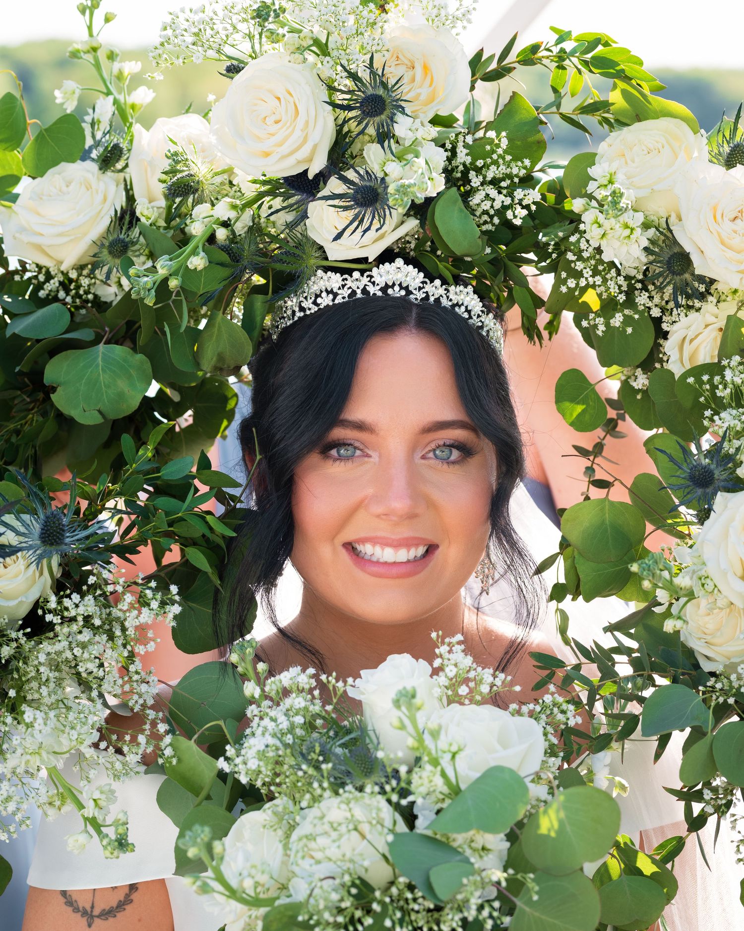 Beautiful bridal portrait framed by an elegant floral arch of white roses, baby's breath, and lush green foliage.