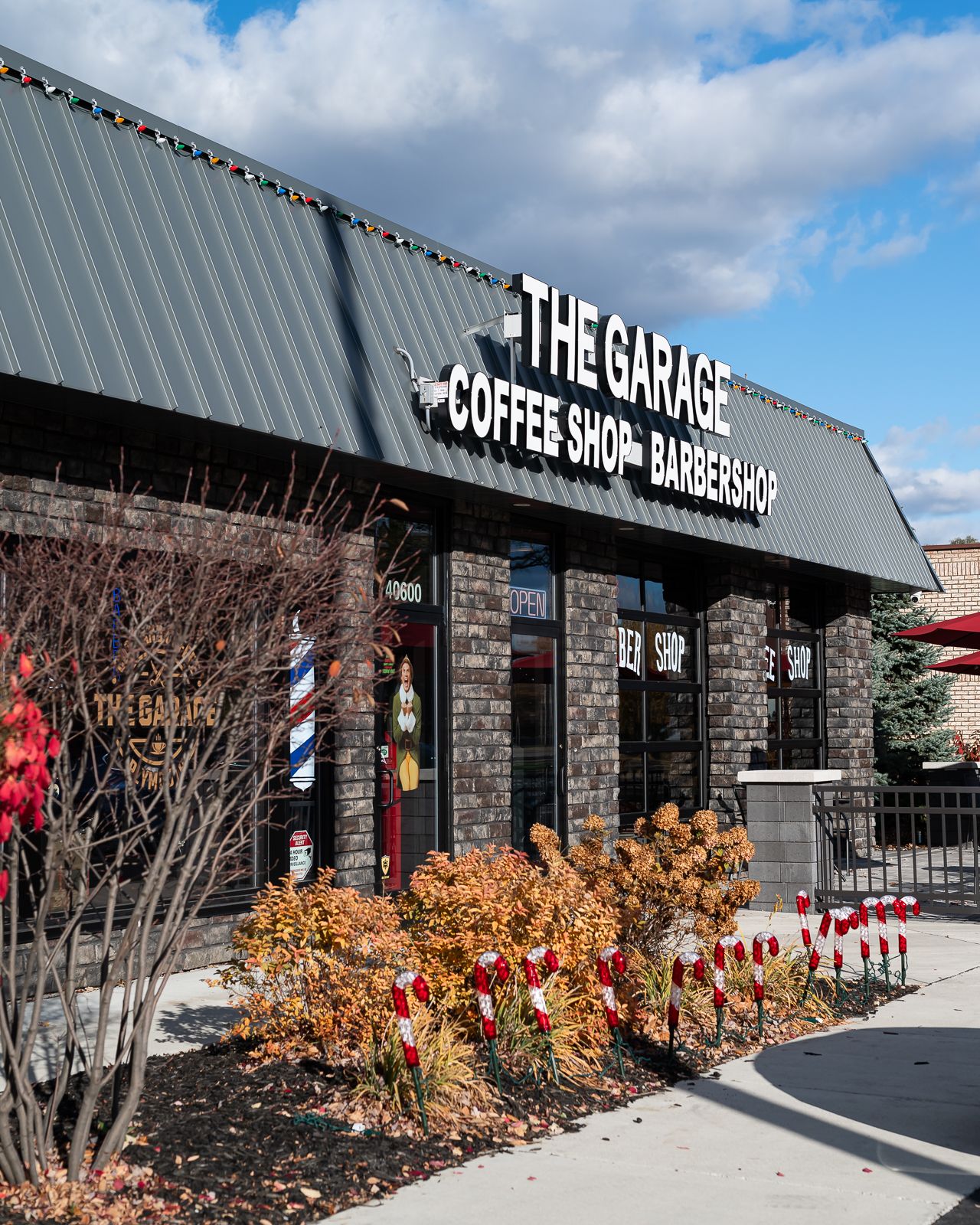 Exterior view of a modern strip mall with coffee shop and barbershop storefronts featuring autumn foliage and stone accents.