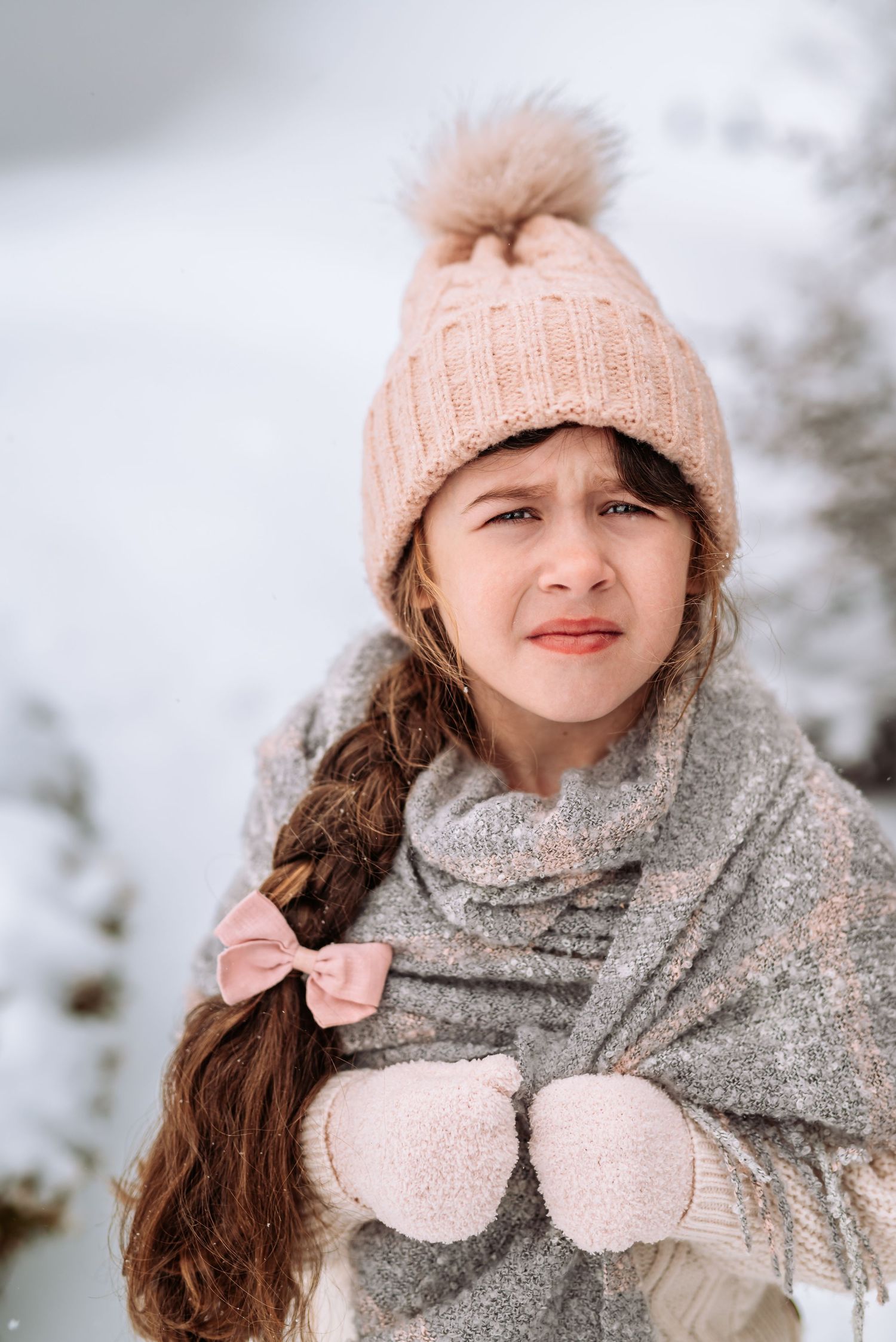 Seasonal winter portrait featuring pink pom beanie, gray sparkly scarf, and hair bow in snowy setting.
