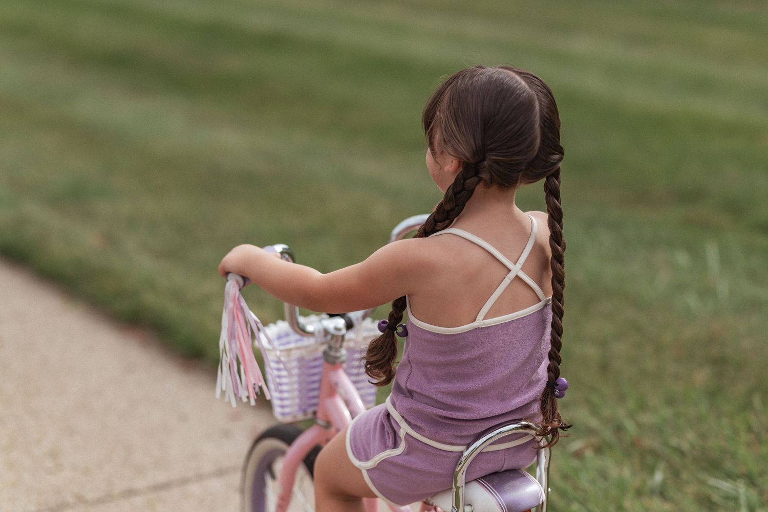 A person in a lavender dress walks along a garden path while reading a book on a sunny day.