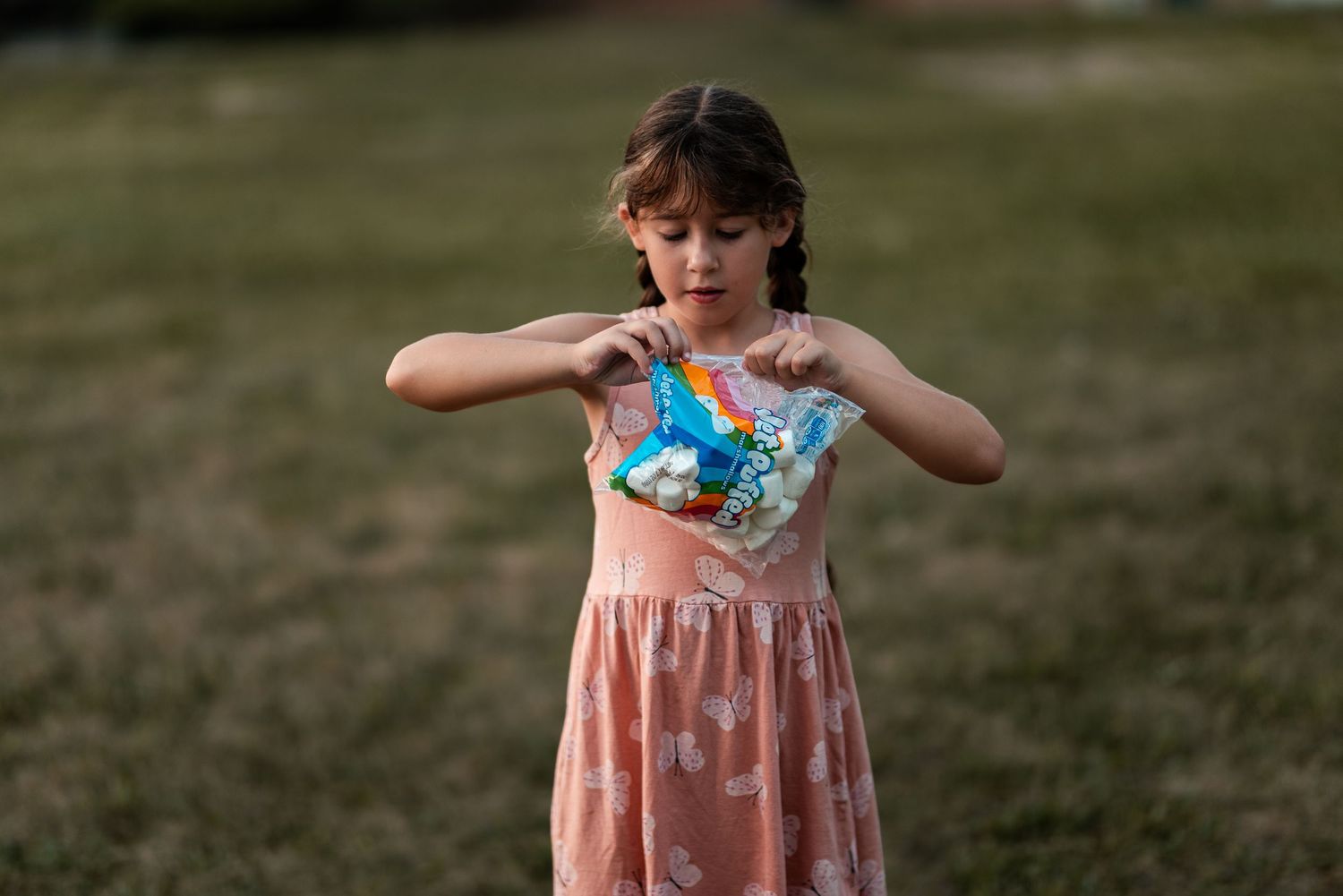 Young girl in pink dress holding a colorful rainbow toy while standing outdoors on green grass.