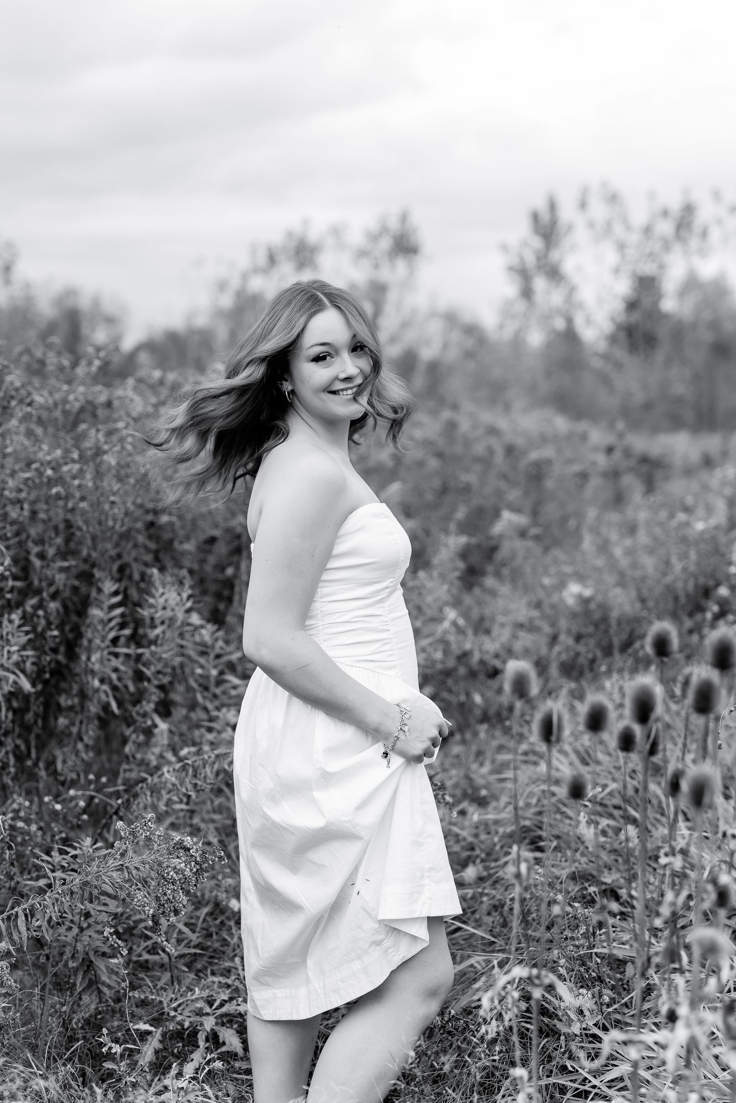 Young woman in white strapless dress smiling in wildflower field, black and white photo.