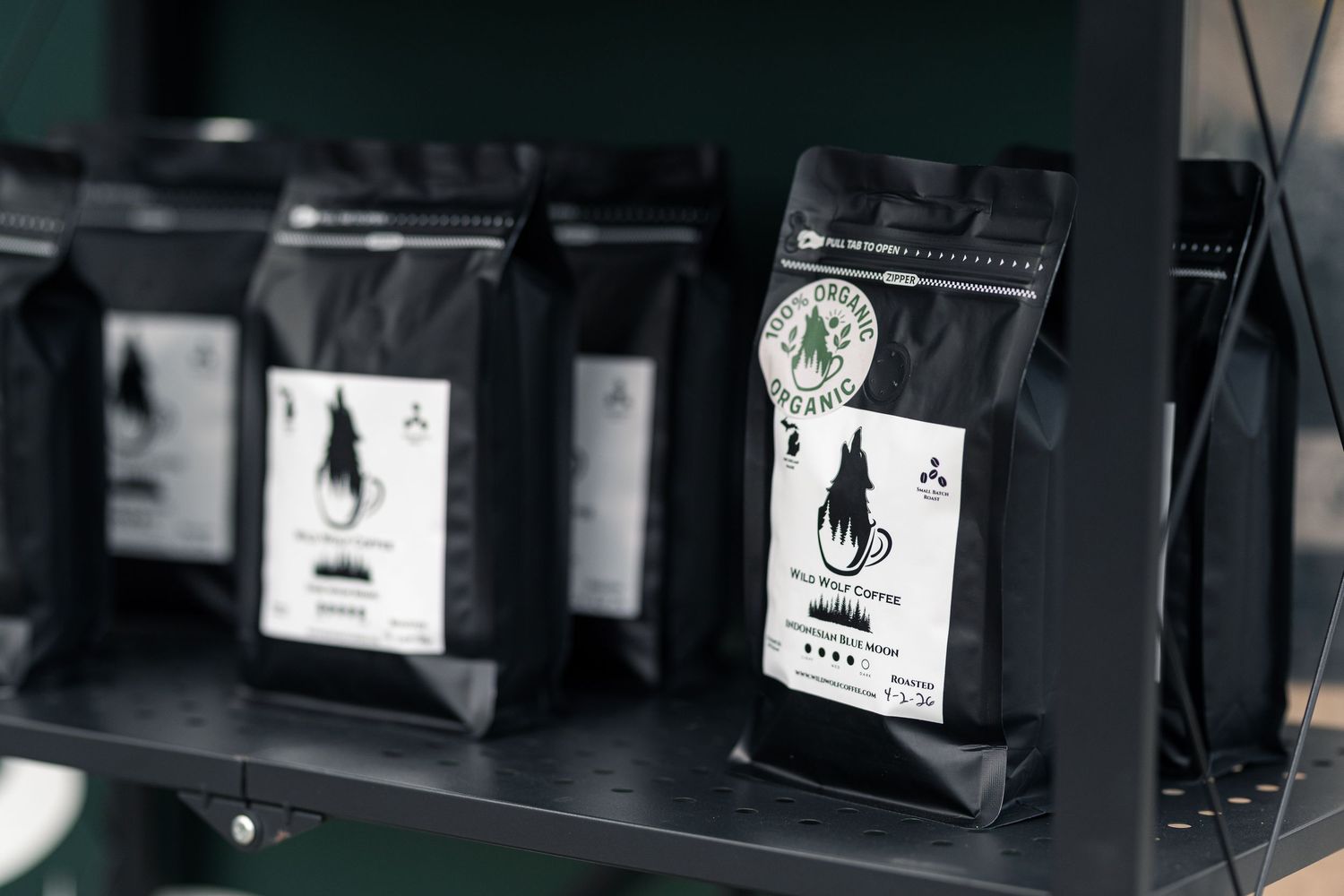 Black coffee bags displayed on a shelf, featuring branded labels with tree logos and product descriptions.
