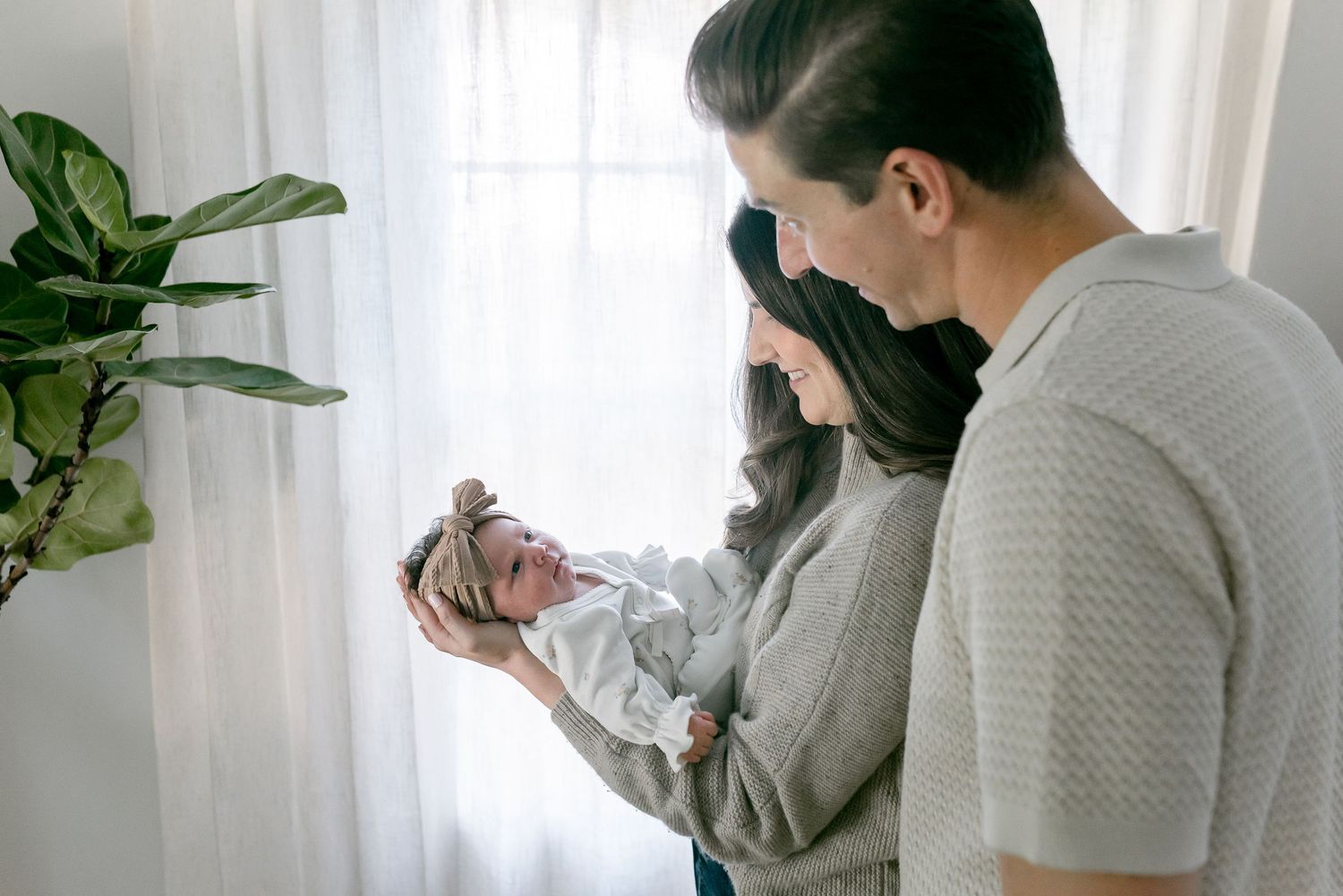 New parents tenderly admire their sleeping newborn baby by a bright window.