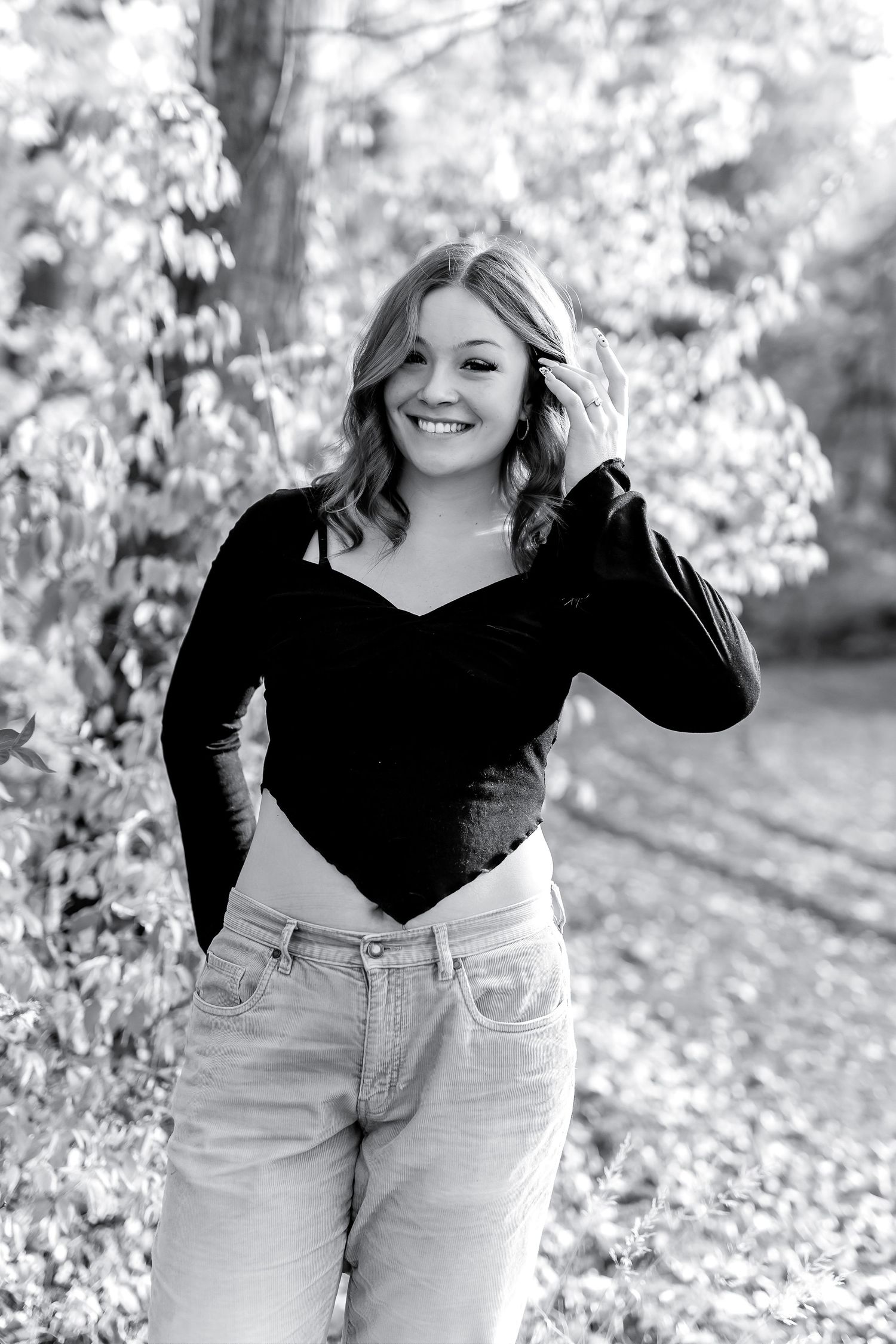 Black and white portrait of smiling blonde woman in black top and jeans outdoors.