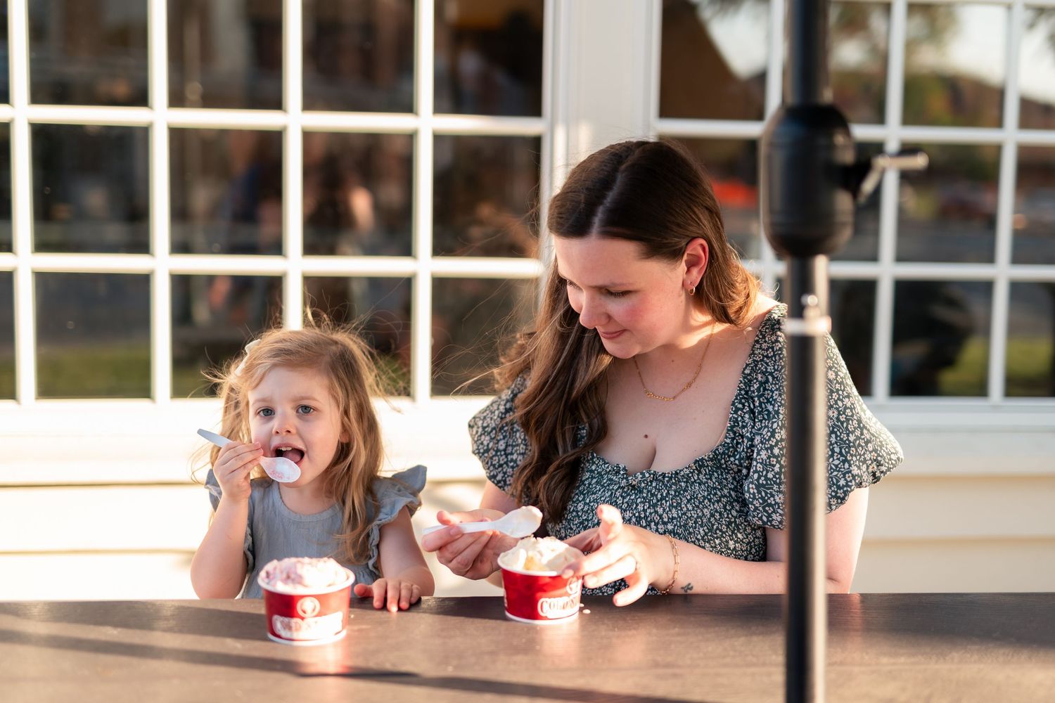 Woman and young girl enjoying ice cream desserts together at an outdoor table in warm evening light.