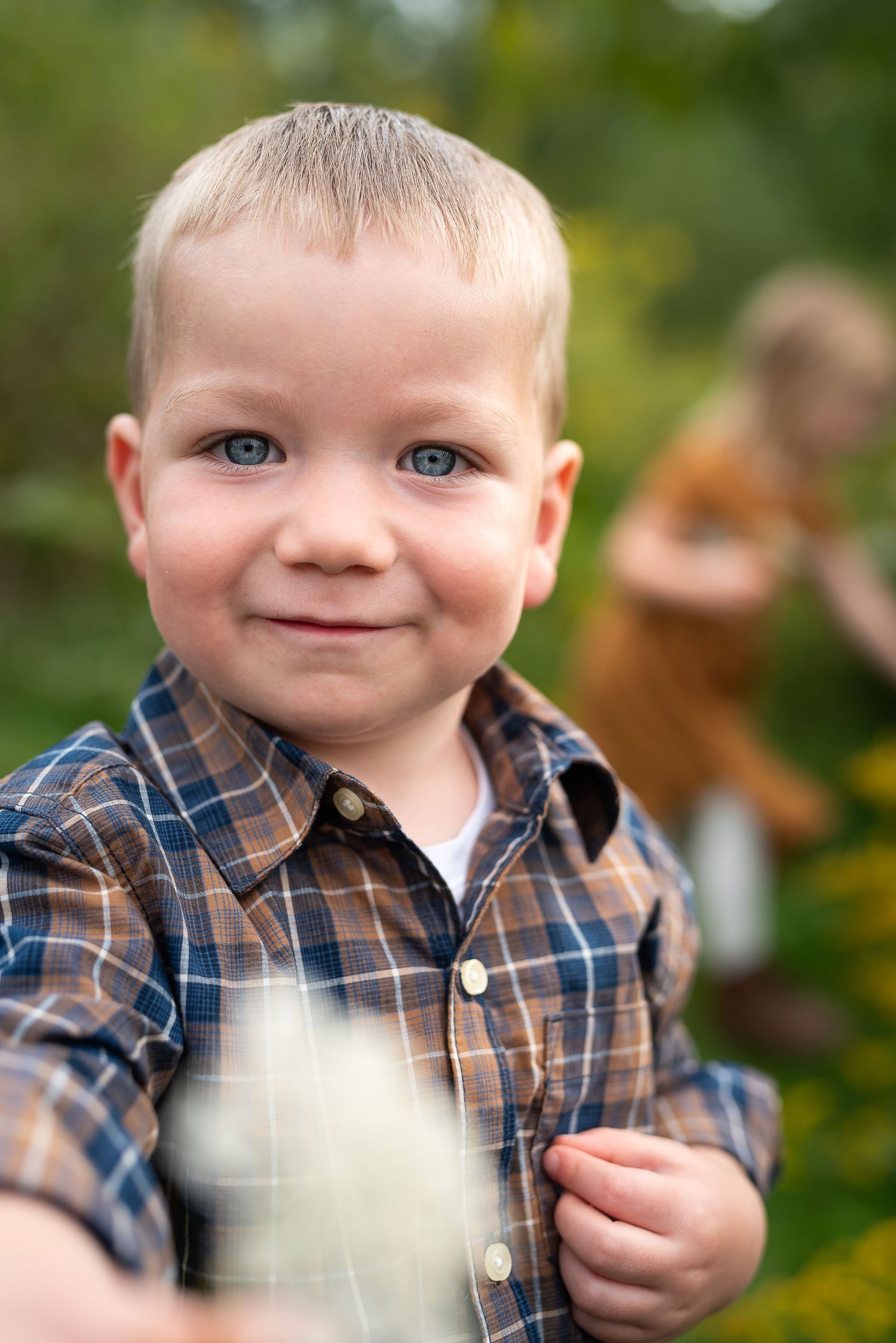 Close up portrait of young child in plaid shirt outdoors with soft bokeh background.