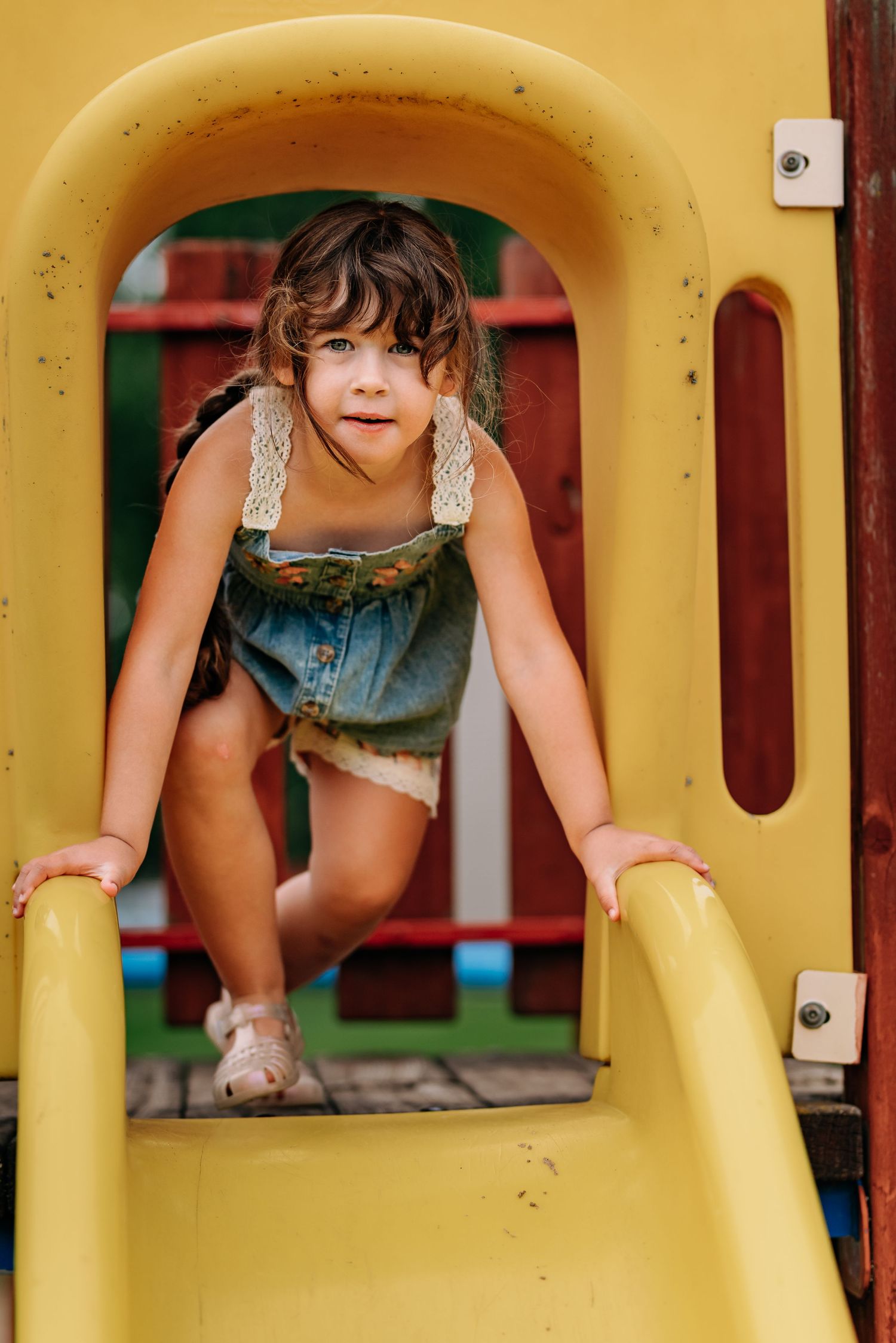 Colorful playground equipment shows a child climbing through a yellow tunnel opening on outdoor play structure.