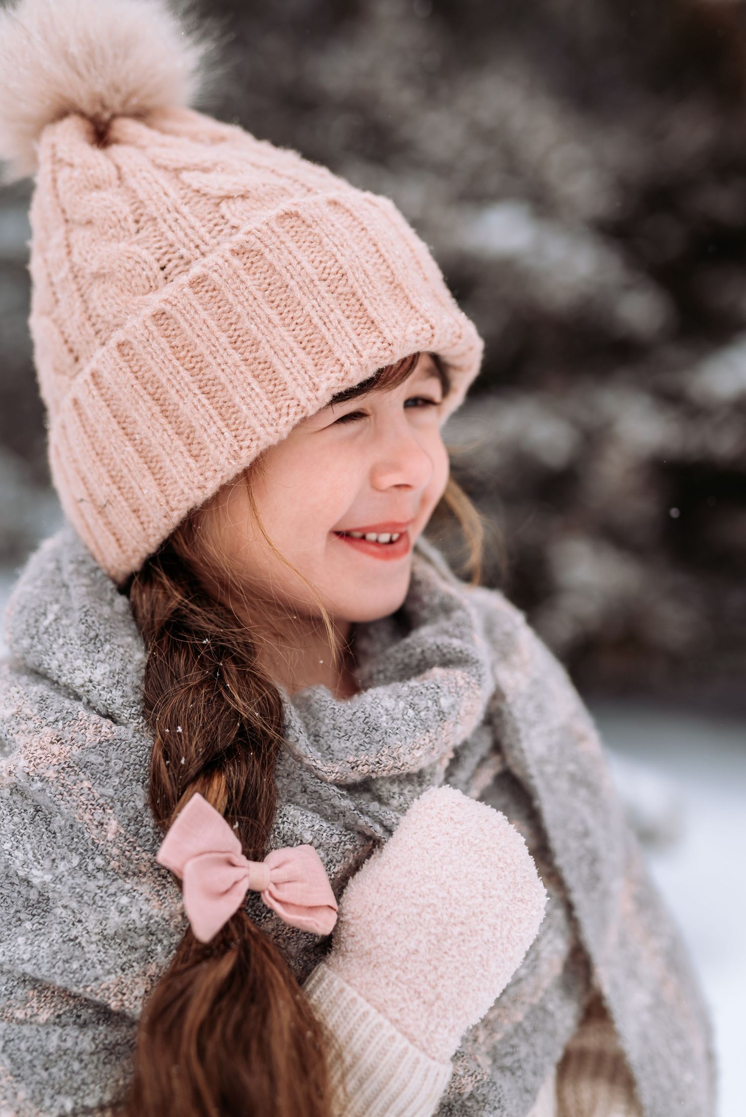 Close-up winter portrait showcasing pink knit hat, gray scarf and delicate bow details.