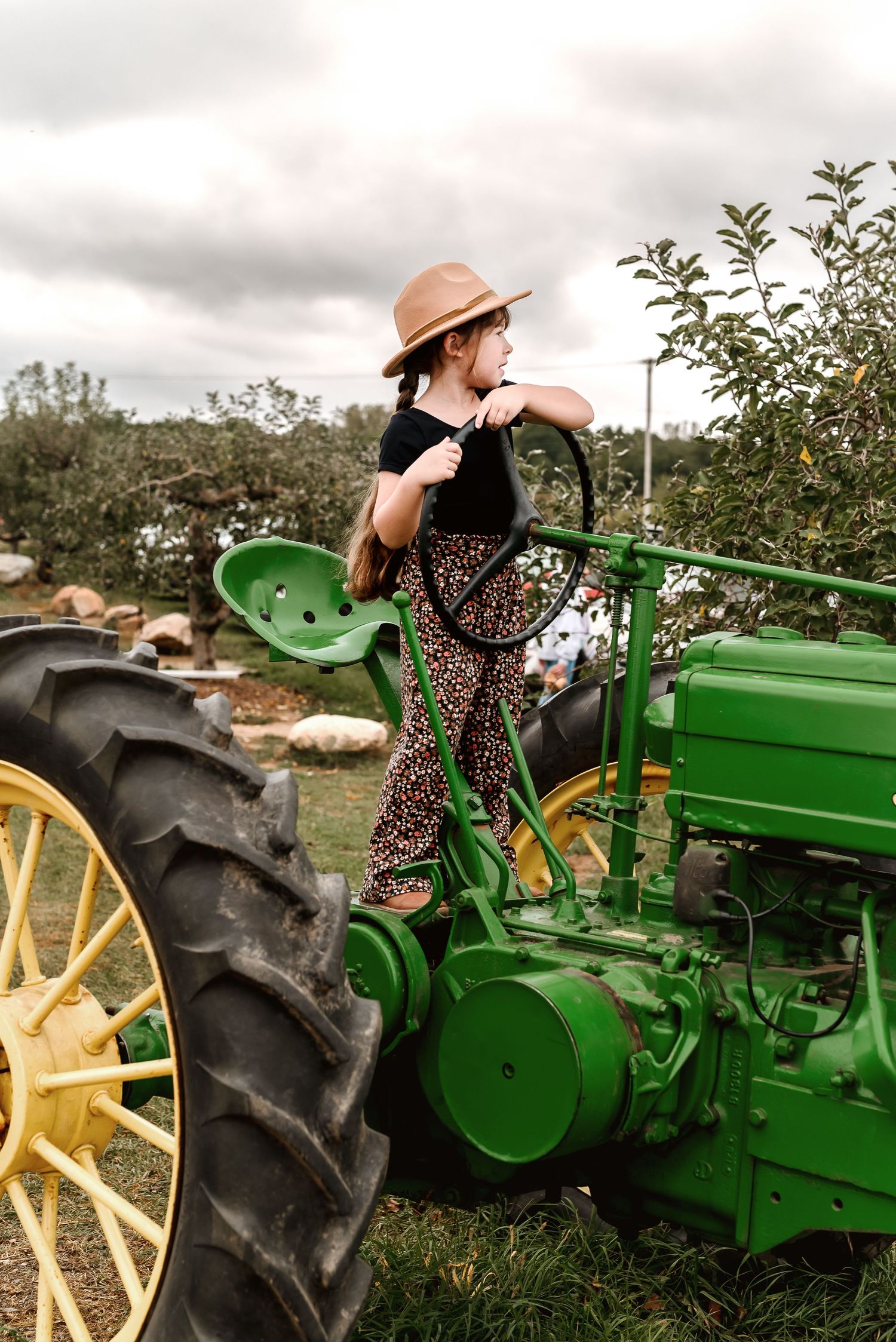 A vintage green John Deere tractor displayed in a field with someone in a polka dot dress posing on it.
