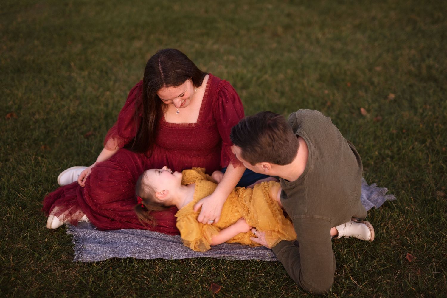 A couple lying on a blanket in the grass share an intimate moment together at sunset.