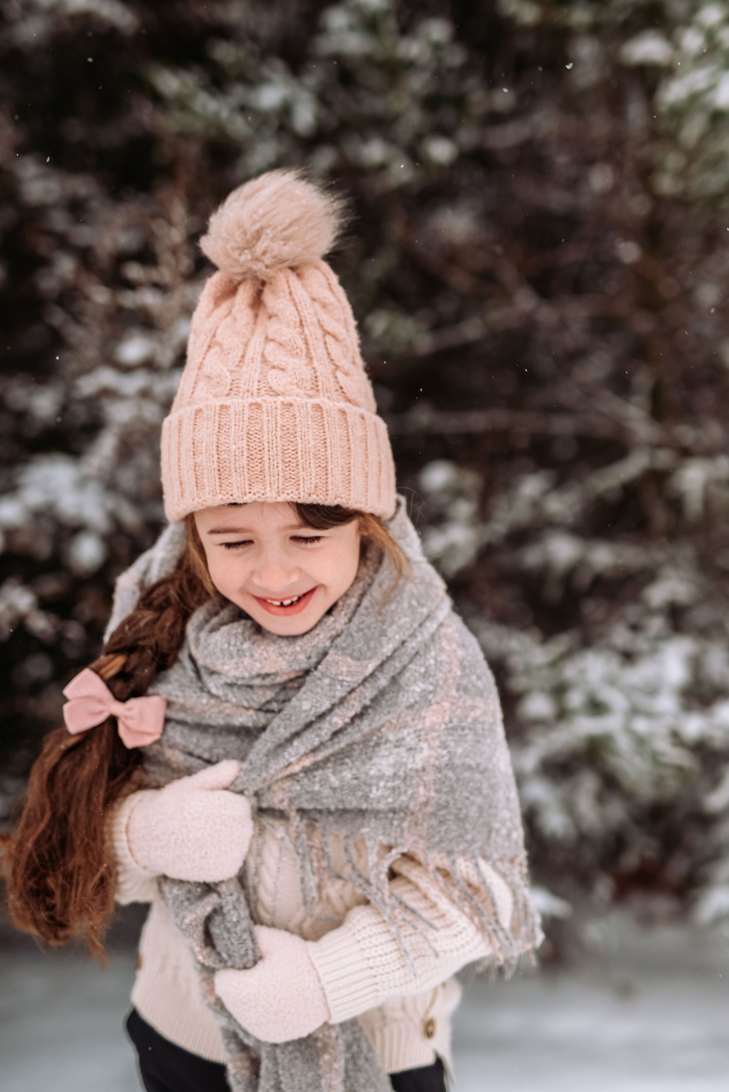 Winter fashion portrait showing pink knit hat, gray scarf, and playful poses against snowy evergreen backdrop.
