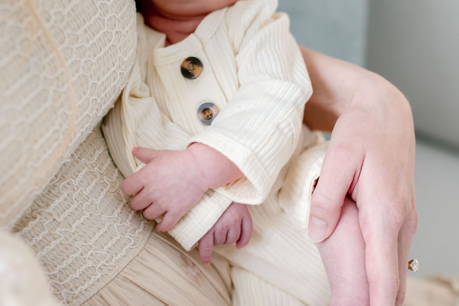 Close-up of newborn baby hands in cream knit cardigan being held by mother.