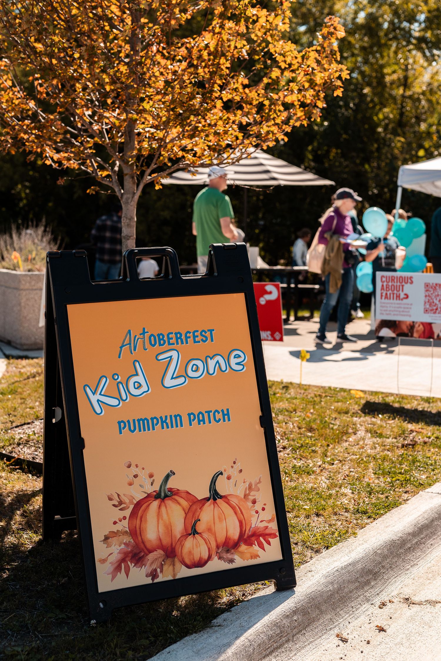 Artoberfest Kid Zone Pumpkin Patch sandwich board sign at a sunny autumn outdoor community event.