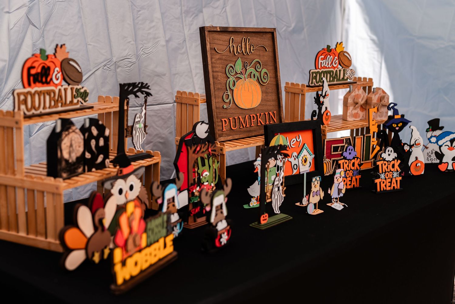 Colorful fall and Halloween themed wooden decorative signs displayed on a table at a craft fair.