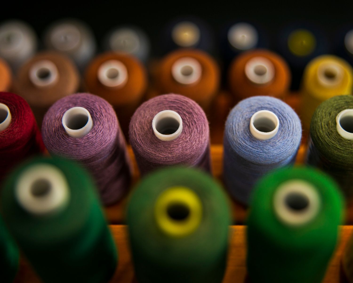 Colorful spools of thread arranged in rows, featuring shades of red, purple, blue, green, and orange for sewing projects.