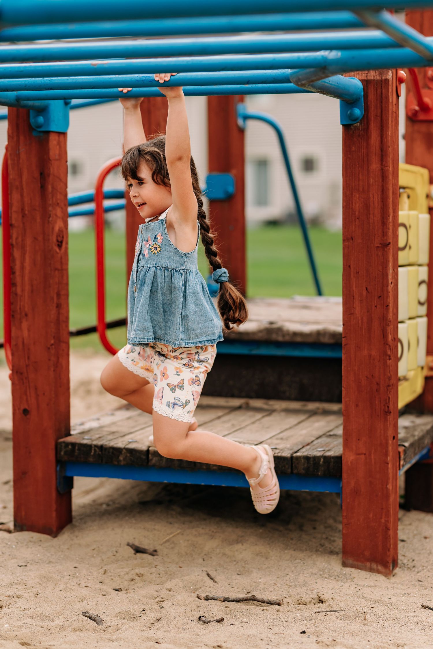 Child climbing and playing under blue playground equipment with wooden supports.