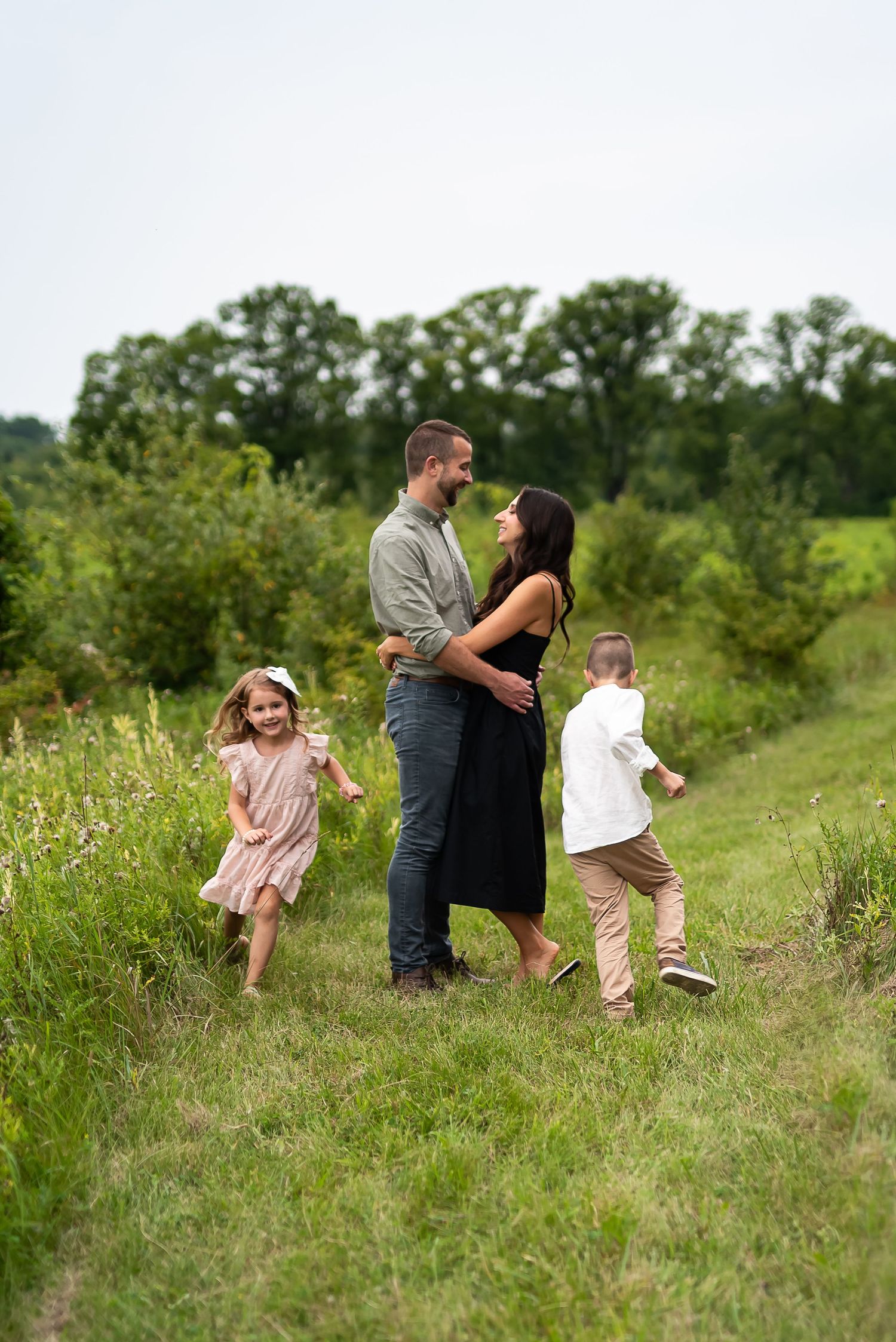 A happy family of four enjoys a sunny day in a lush green meadow, with two young children running toward their parents.