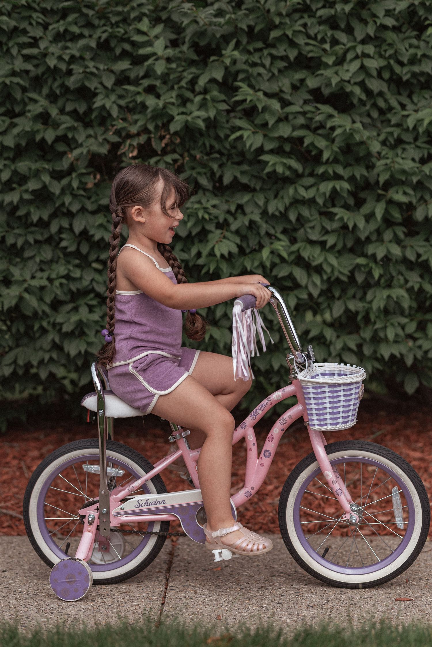 A series of four progressive photos showing a child mounting and riding a pink and white bicycle with training wheels.