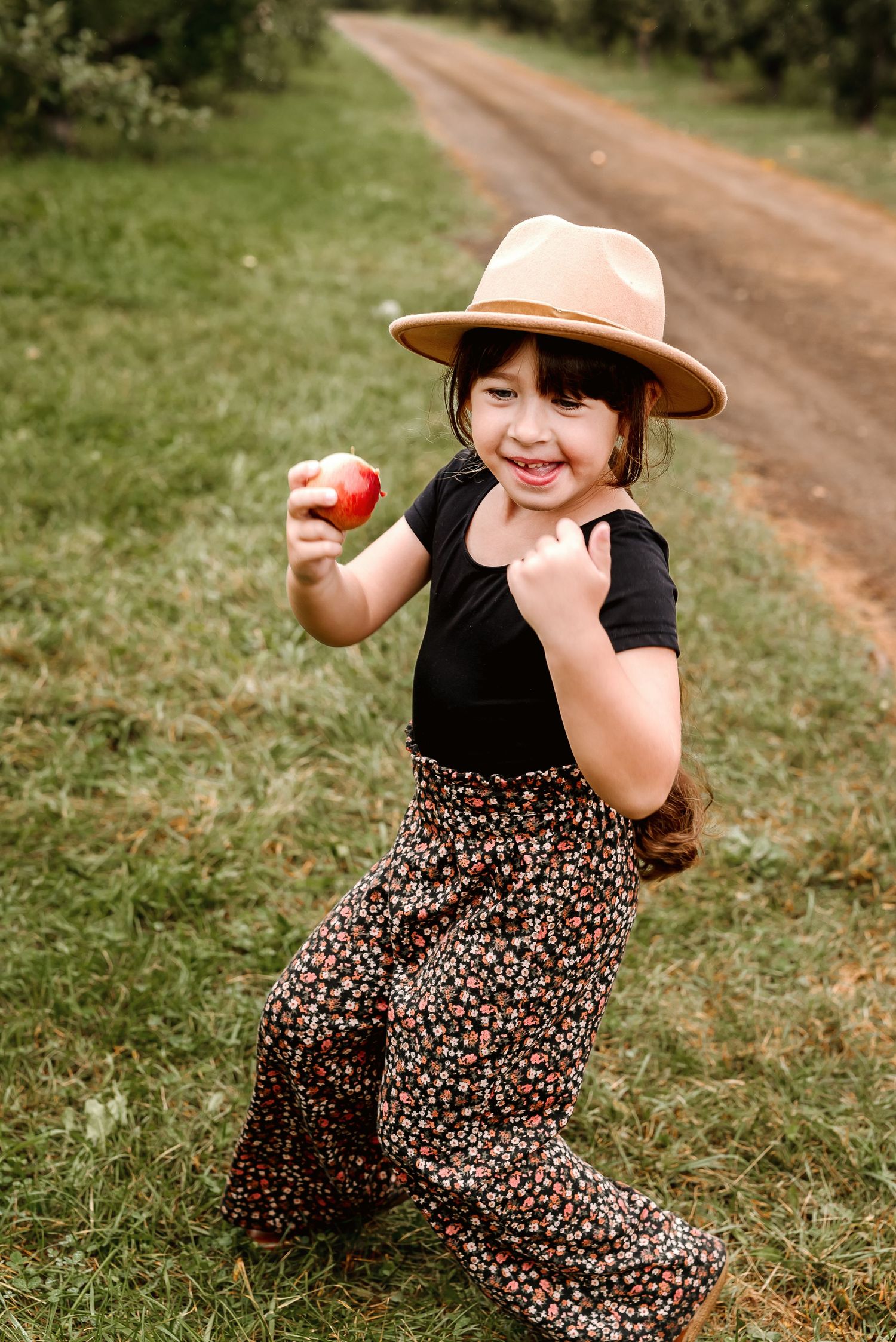 A series of playful outdoor photos showing someone in a floral dress and peach hat sitting on grass near a dirt path.