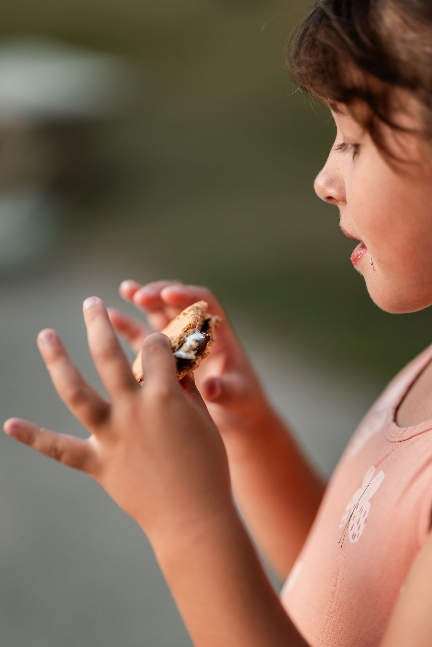 Young child holding and eating a gooey s'more with melted marshmallow and chocolate between graham crackers.