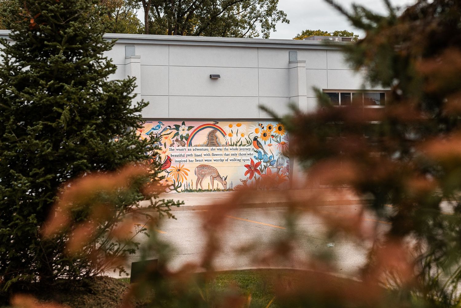 Colorful mural on school building exterior featuring animals and rainbow, framed by autumn trees in foreground.