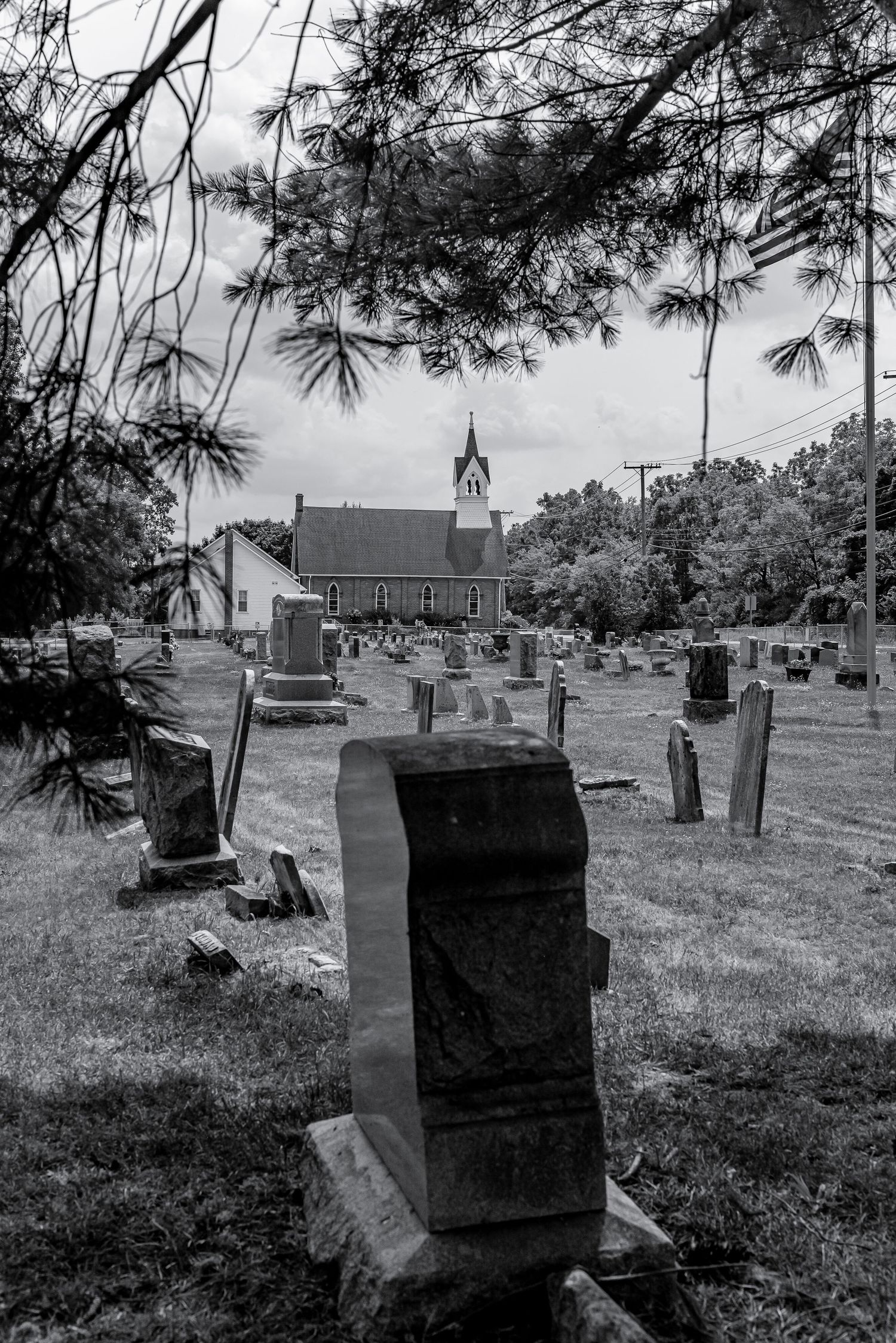 Black and white photo of an old cemetery with gravestones leading to a historic church surrounded by trees.
