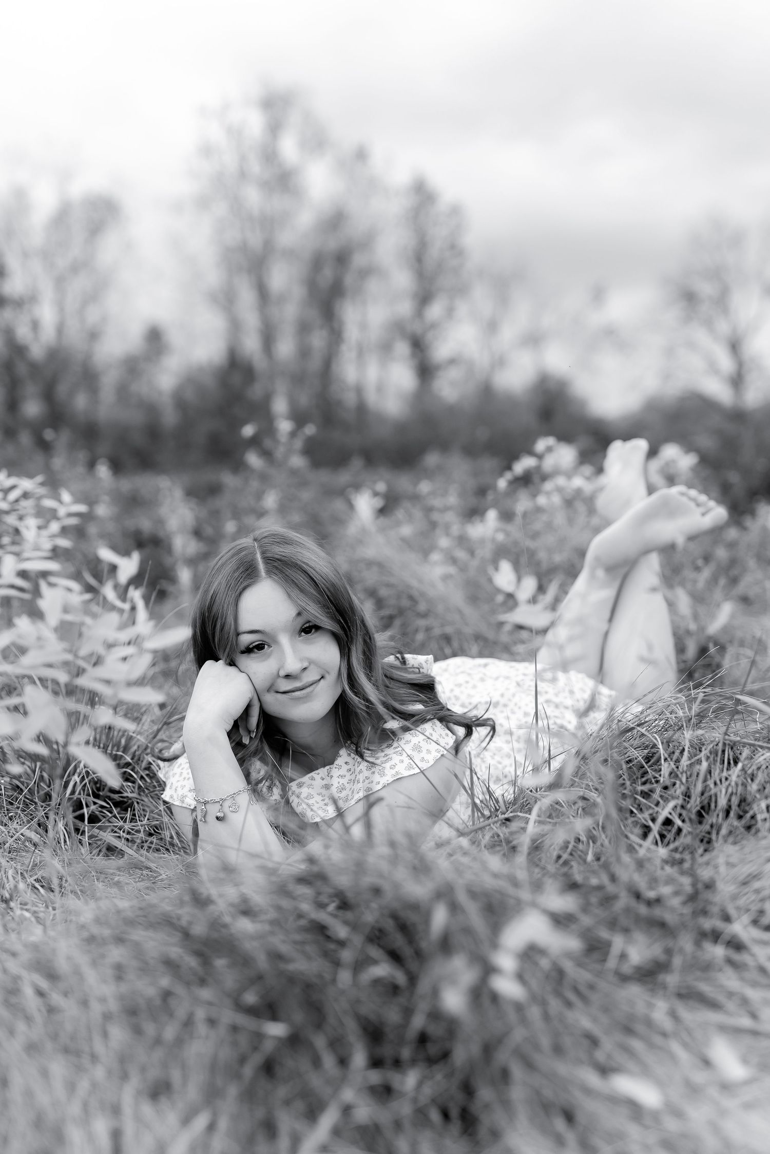 Black and white portrait of young woman lying in grass field smiling at camera.