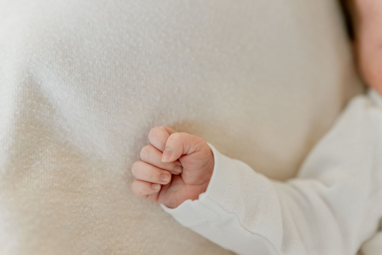 Close-up of a newborn baby's tiny fist gently gripping a soft white knit blanket.
