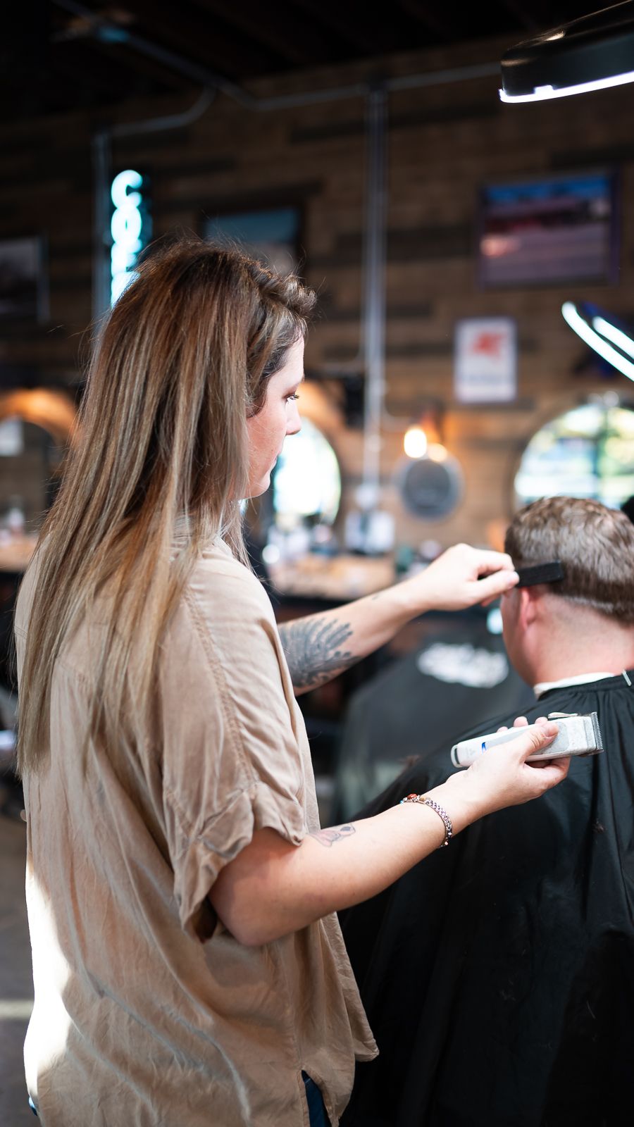 Hairstylist in beige shirt cutting client's hair in a dimly lit salon setting.