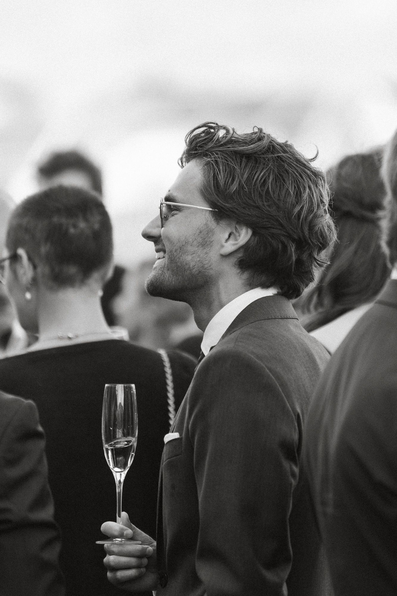 A black and white photo of people in formal attire at a social gathering holding champagne glasses.