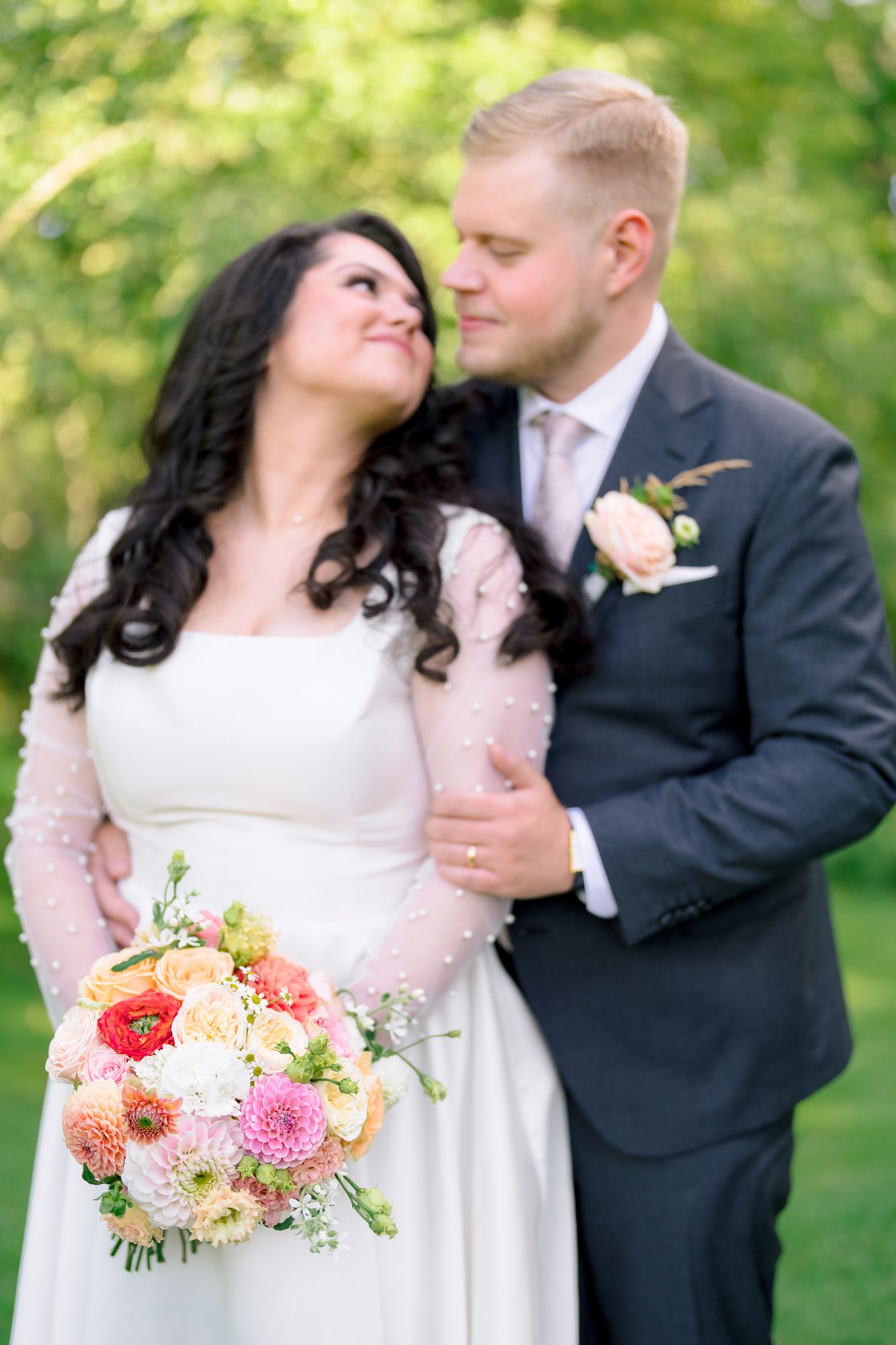 Romantic wedding portrait of couple in garden setting with bride holding coral and pink floral bouquet.
