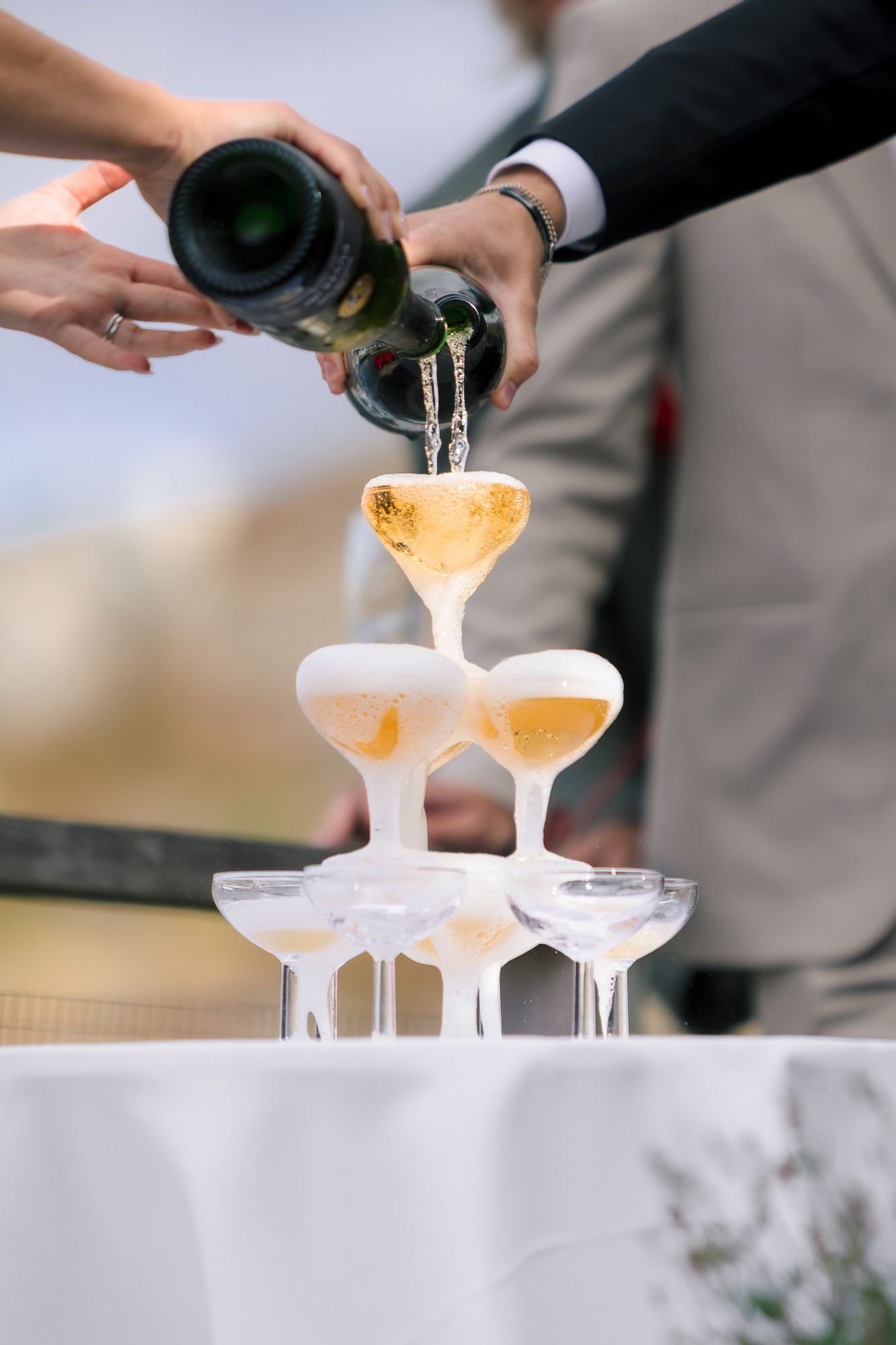 Champagne being poured into a tower of elegant coupe glasses for a celebratory event.