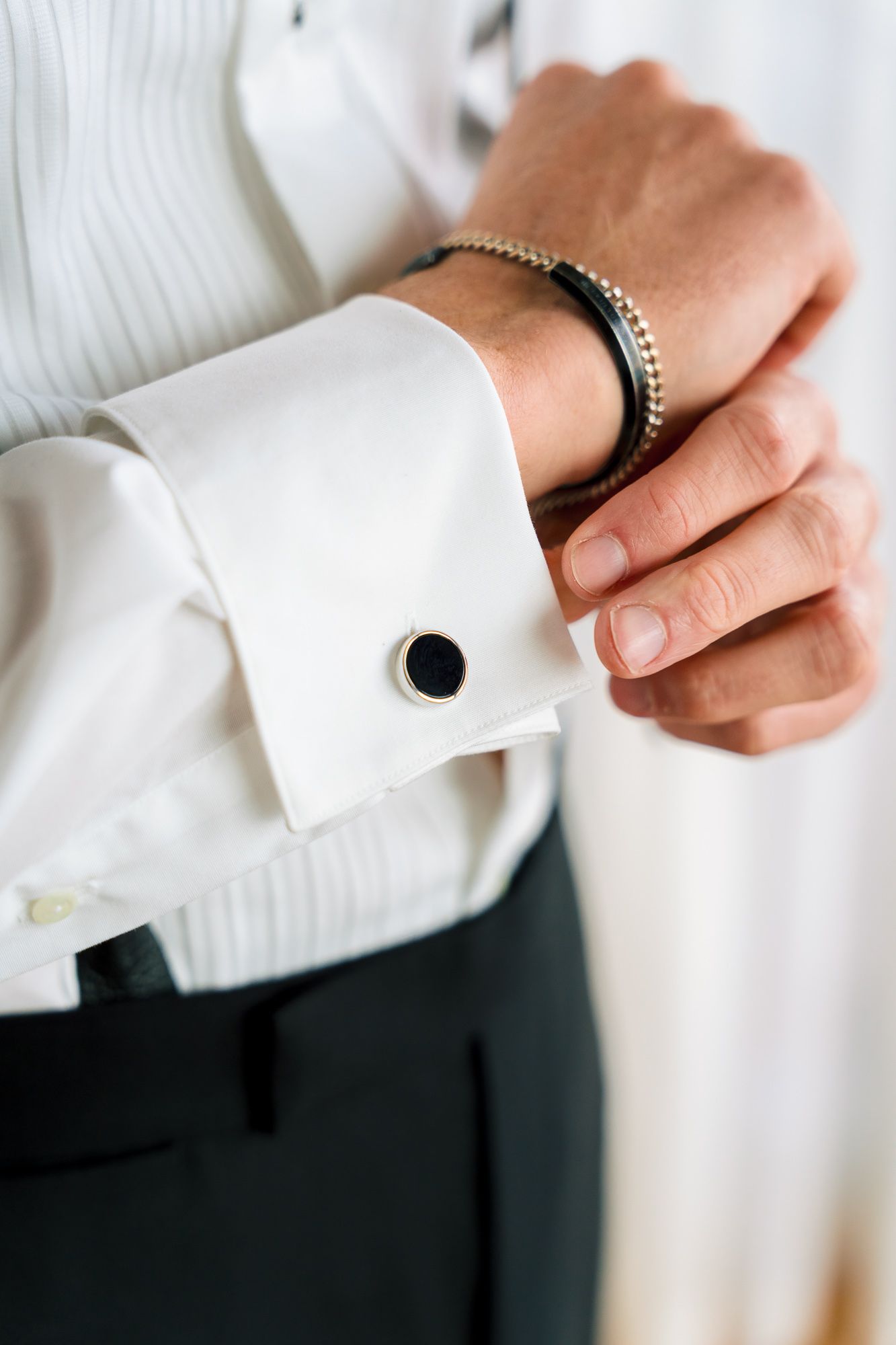 Close-up of hands adjusting white dress shirt cuff with silver cufflinks against dark background.