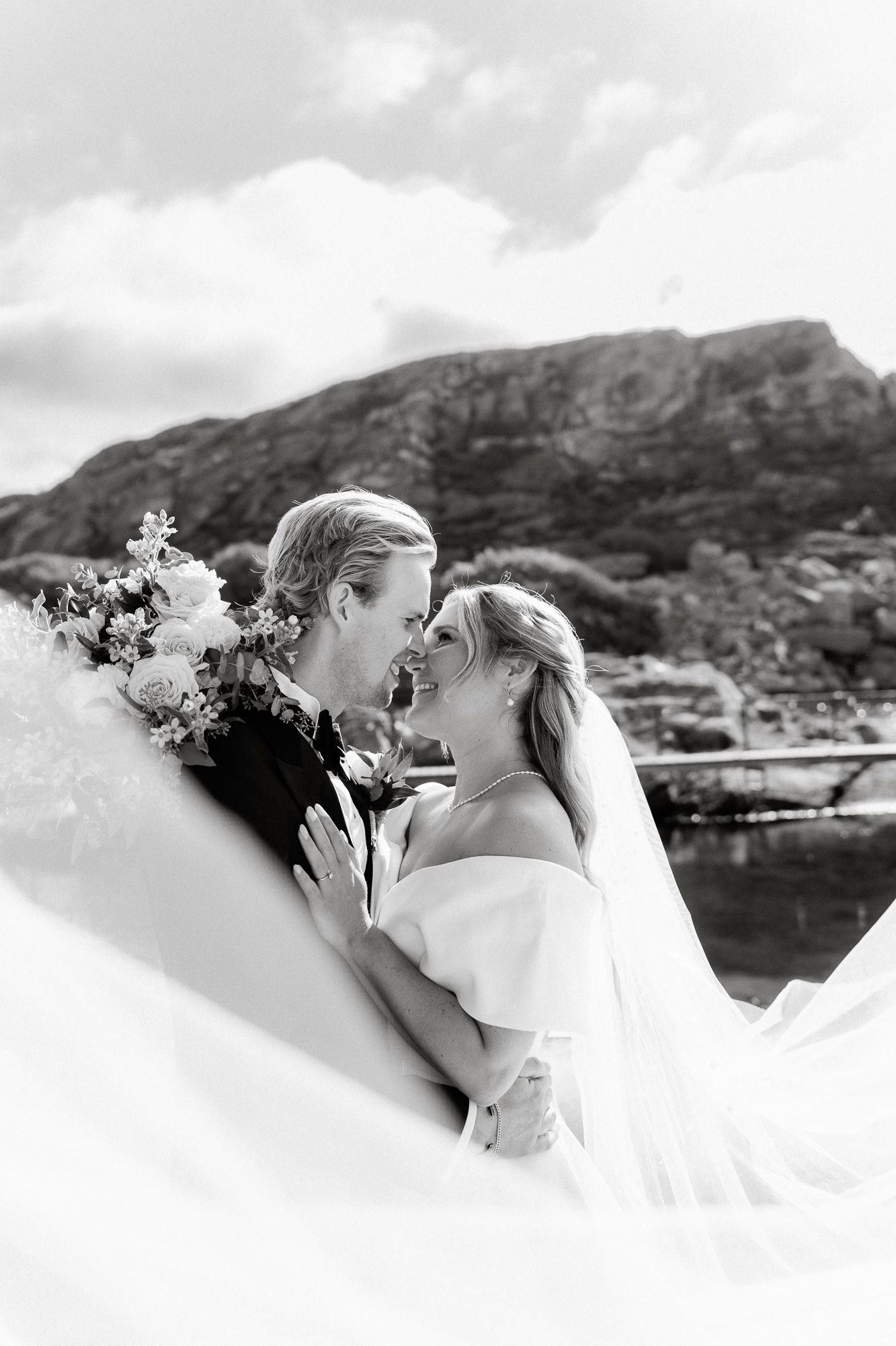 A romantic wedding couple shares a kiss against a scenic mountain backdrop in Hawaii.