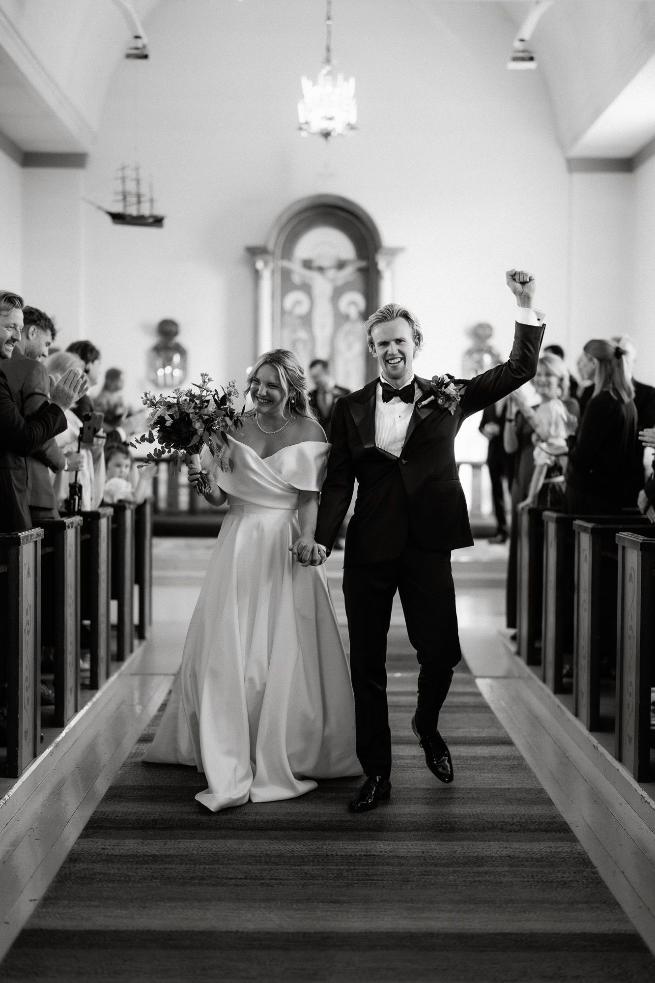 A joyous wedding couple celebrates while walking down the church aisle after their ceremony in black and white.