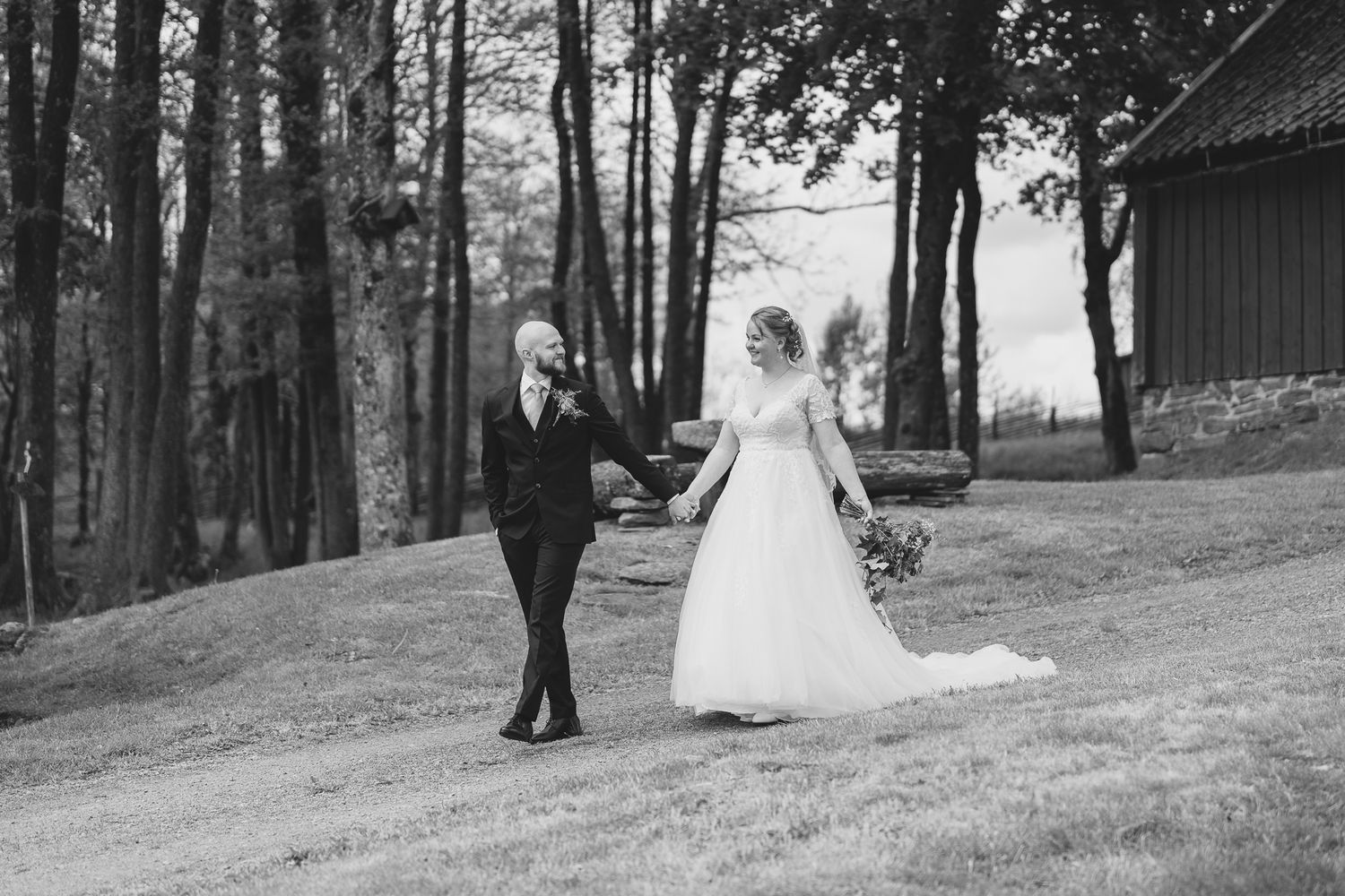 A black and white wedding photo with couple holding hands while walking through a forest path on their special day.