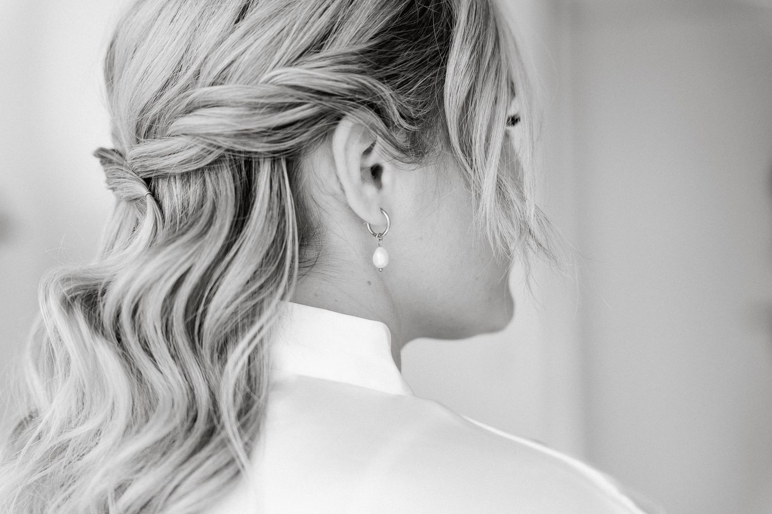 A bride with elegant blonde curls and pearl earrings is shown in profile view against a light background.
