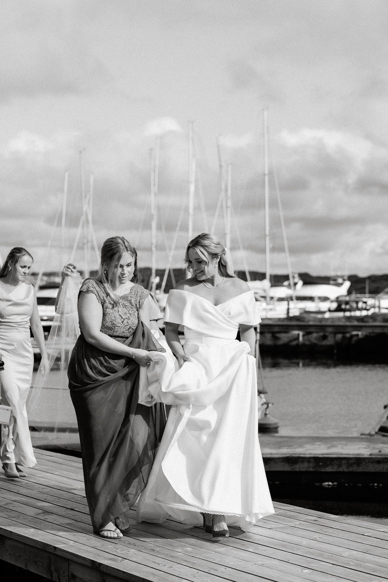 A series of black and white photos showing a wedding dress being blown by wind on a marina dock.