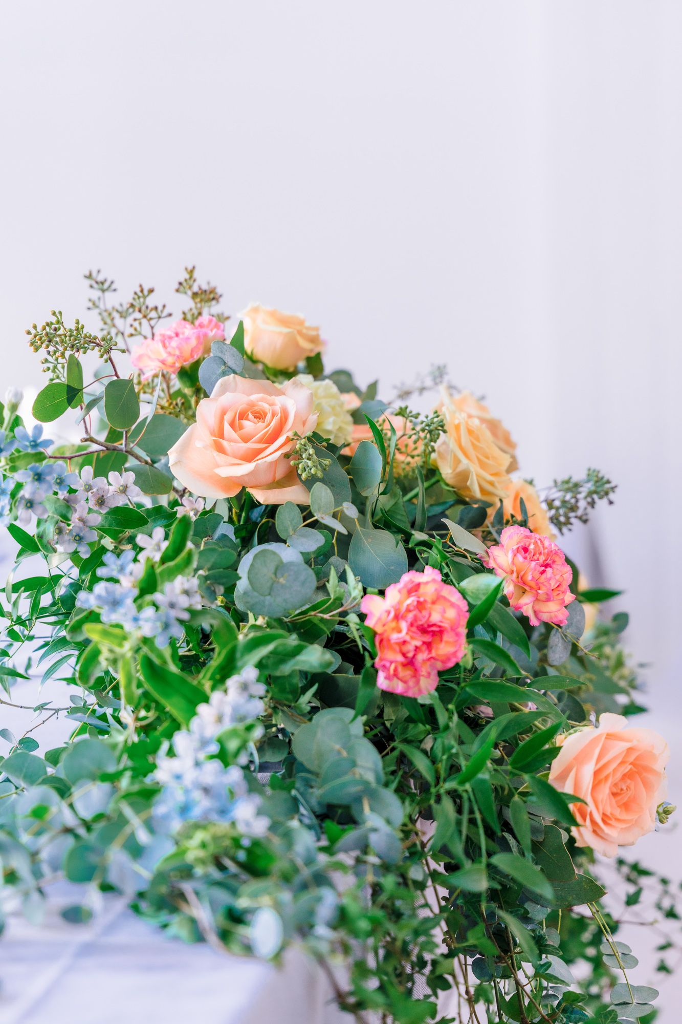 Delicate peach roses and pink carnations arranged with eucalyptus and greenery against a light background.