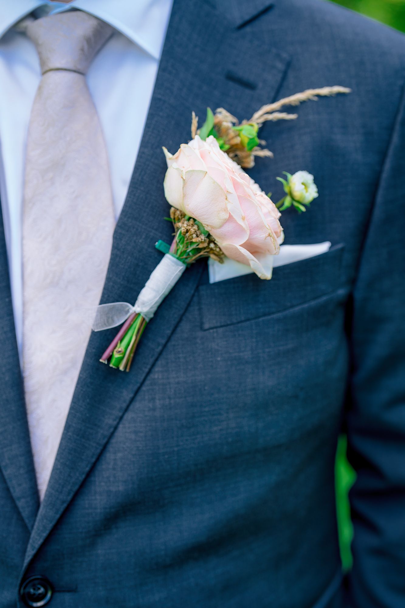 Close-up view of elegant pink rose boutonnieres pinned to dark navy suit jackets at a formal wedding.