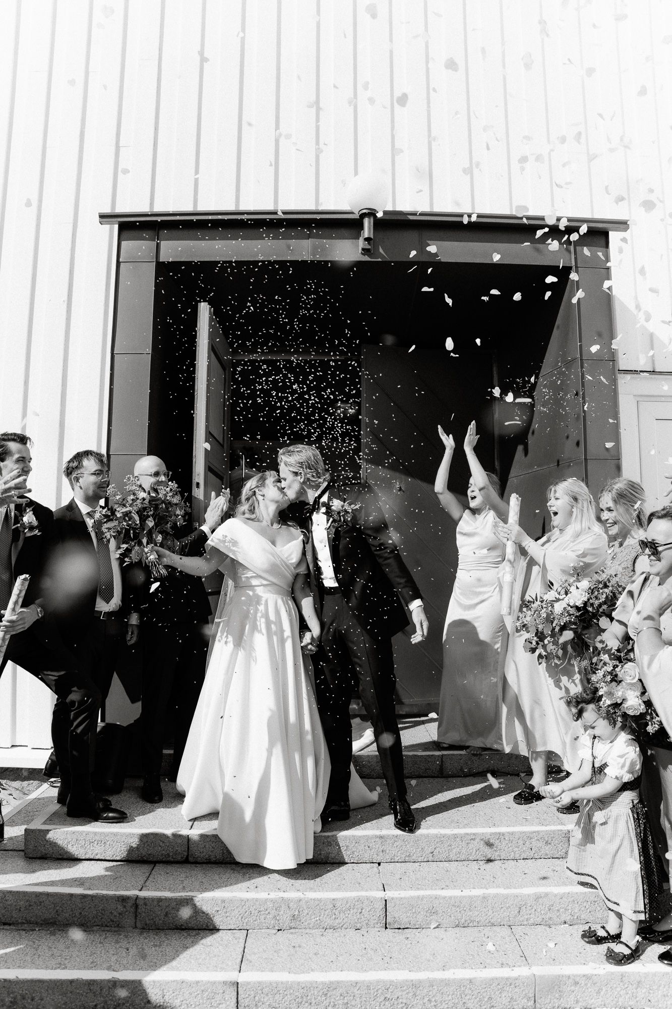 A black and white wedding sequence showing people exiting a building and celebrating with bubbles and confetti.