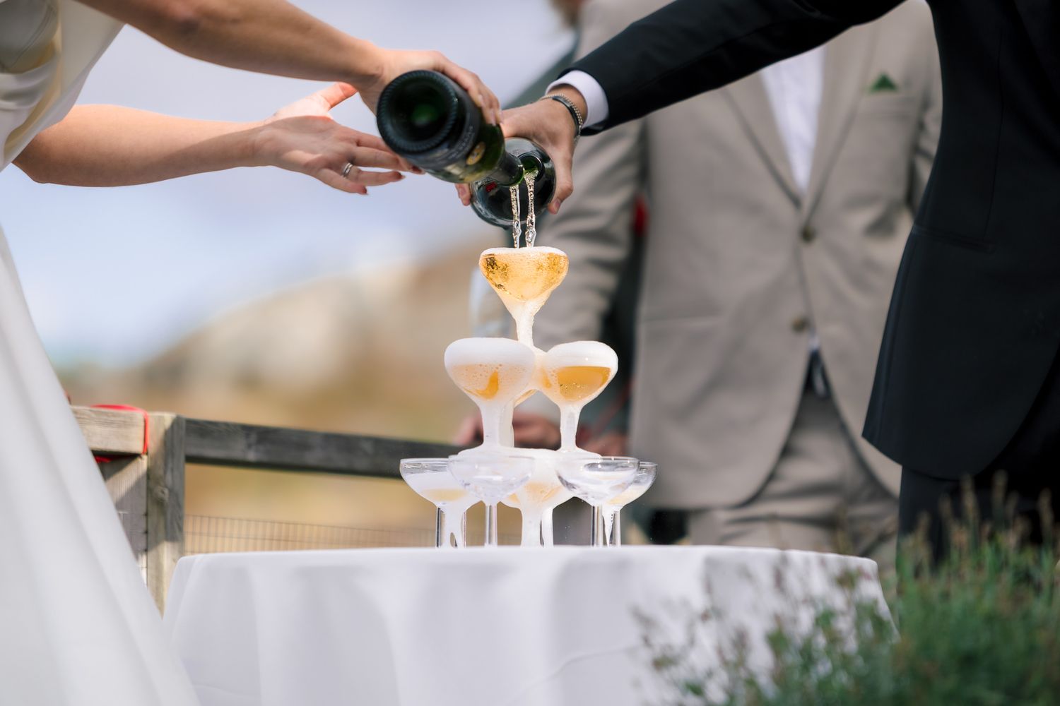 Champagne being poured into elegant tower of glasses at an outdoor celebration.