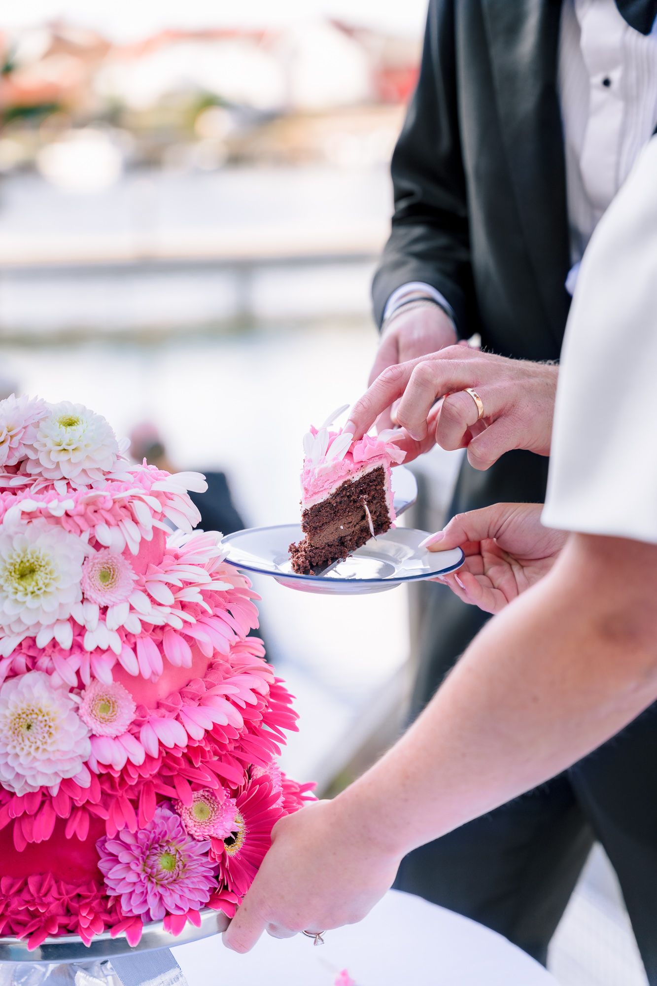 A series of hands serving pink gerbera daisy decorated chocolate cake slices at an elegant event.