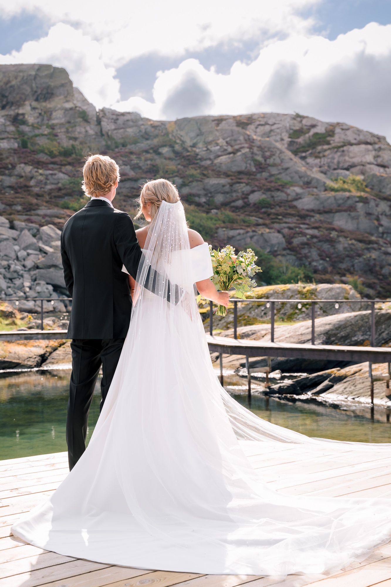 Newlywed couple stands together overlooking scenic mountain lake view in romantic wedding photography series.
