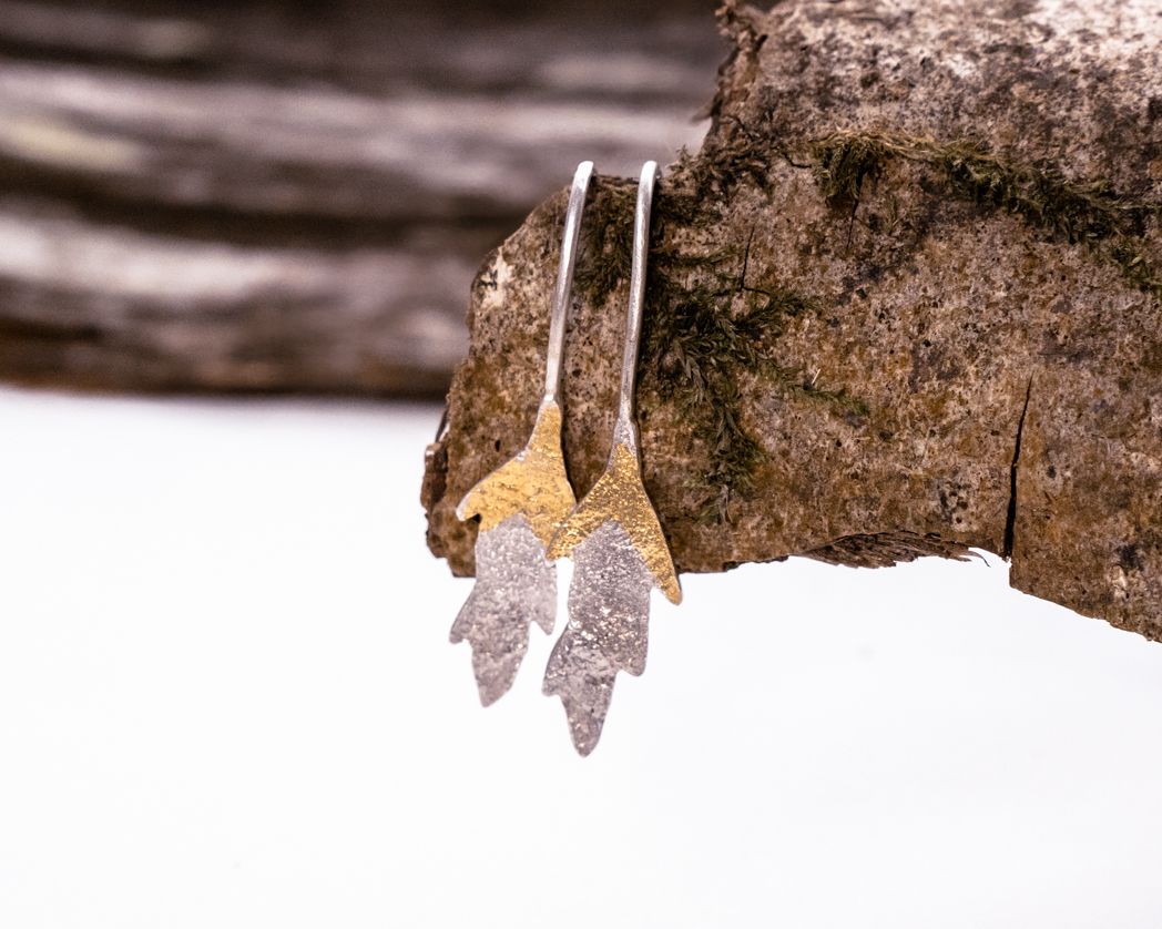 Silver leaf-shaped earrings dangling against a snowy winter backdrop.