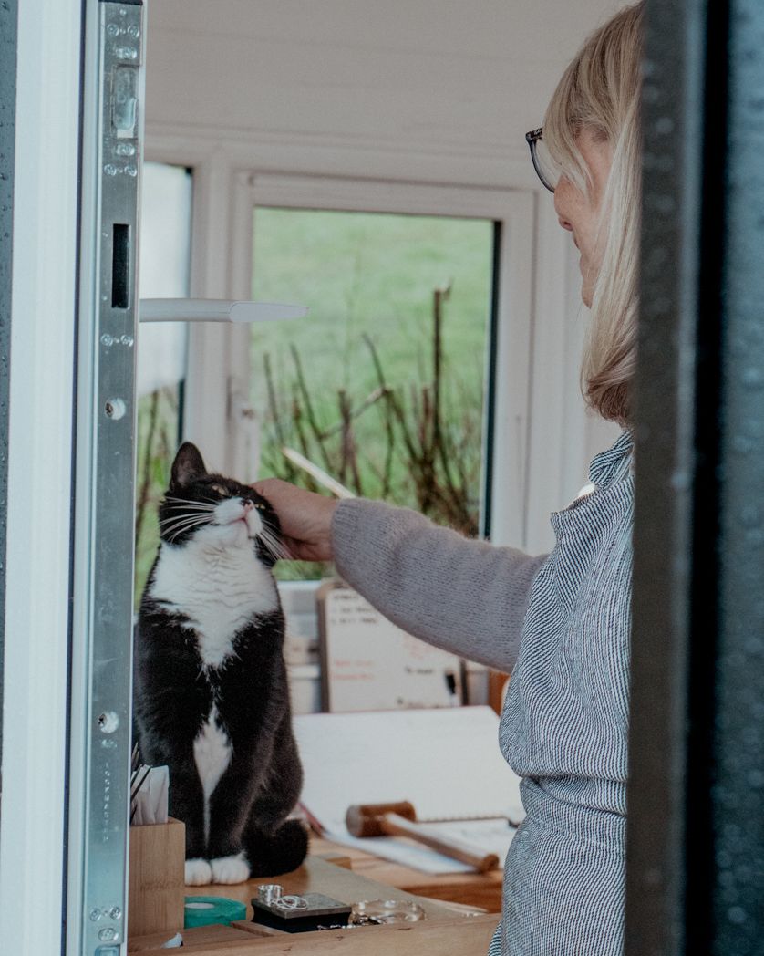 A black and white cat receives attention at a jewelry workbench.